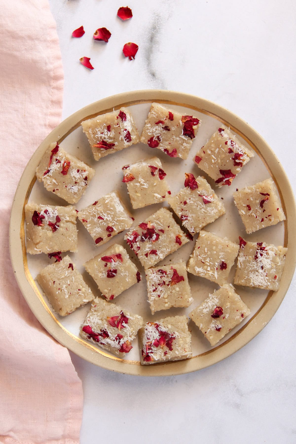 kaju makhana burfi garnished with coconut and dried rose petals on a white platter. 