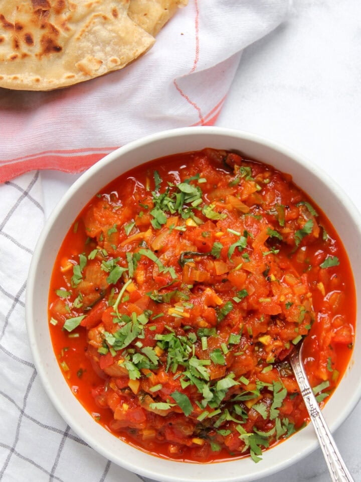 Tomato chutney in a white bowl garnished with cilantro.