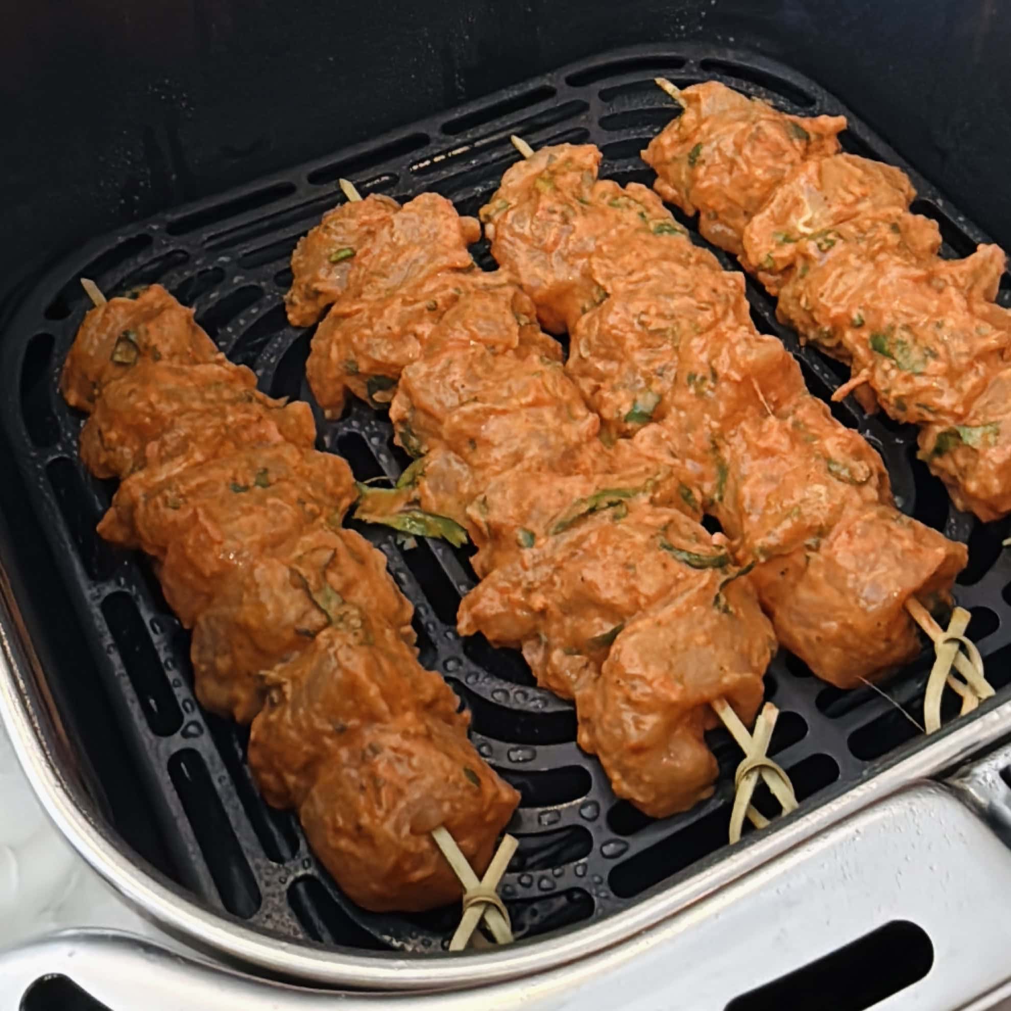 Four skewers of marinated chicken are placed inside an air fryer basket, ready to be cooked.