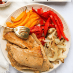 Un plato con rodajas de kebab de pollo con pimientos amarillos y rojos cocidos, cebolla, un tenedor dorado y tazones pequeños de salsas verdes y rojas.