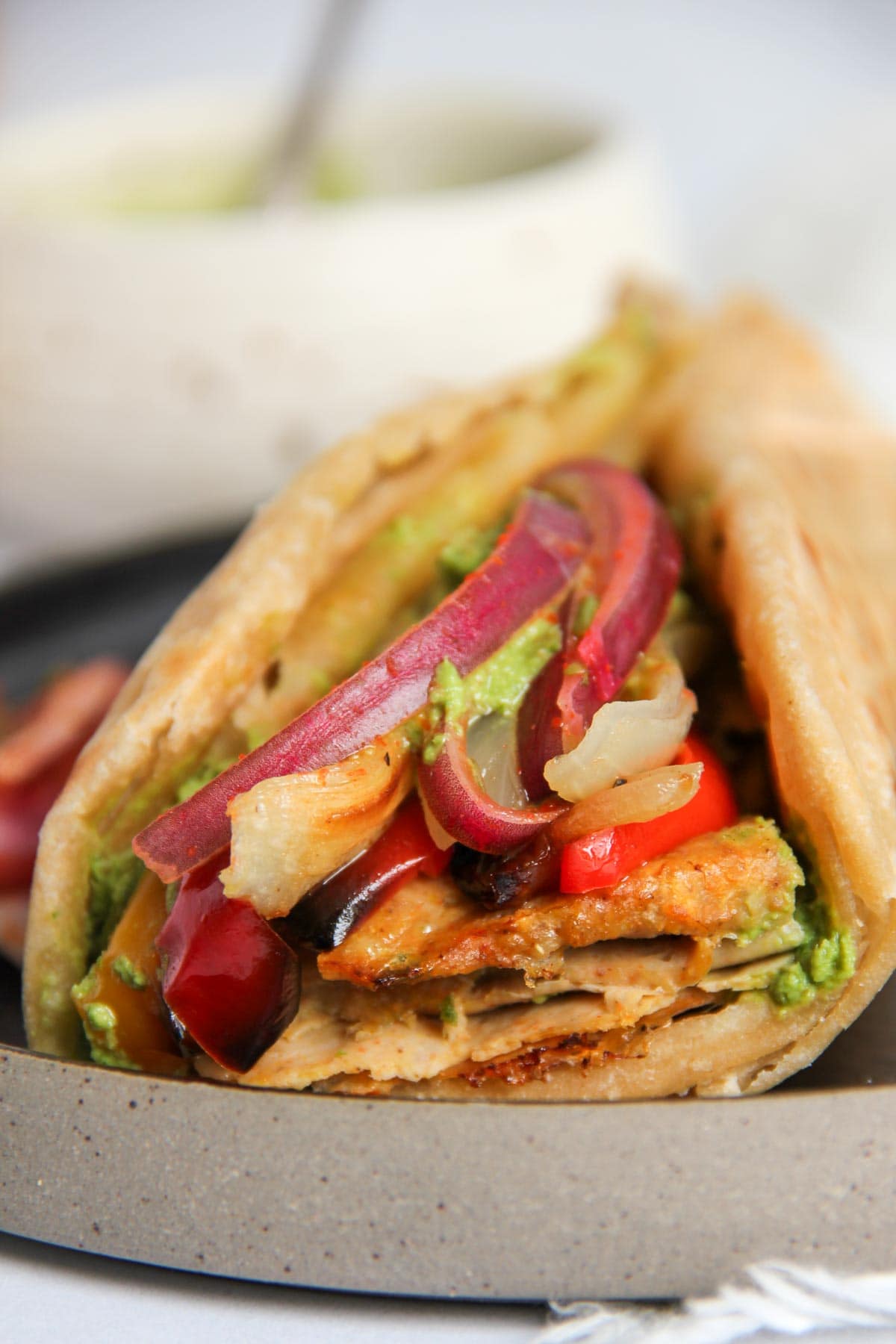 Un primer plano de un sándwich relleno de verduras asadas, cebollas rojas y salsa verde, servido en un plato de cerámica.