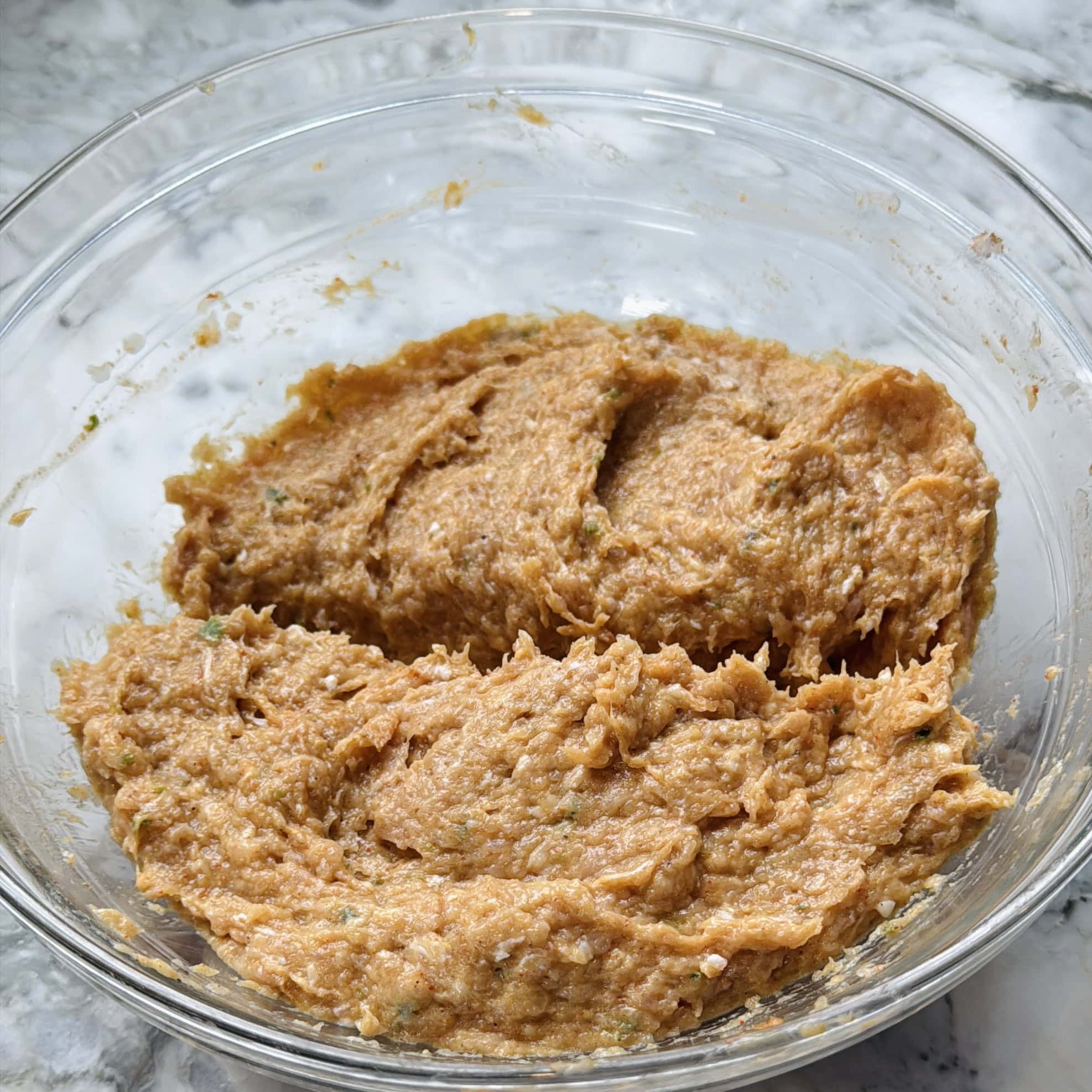 Un recipiente de vidrio lleno de una mezcla espesa de color marrón anaranjado sobre una superficie de mármol.