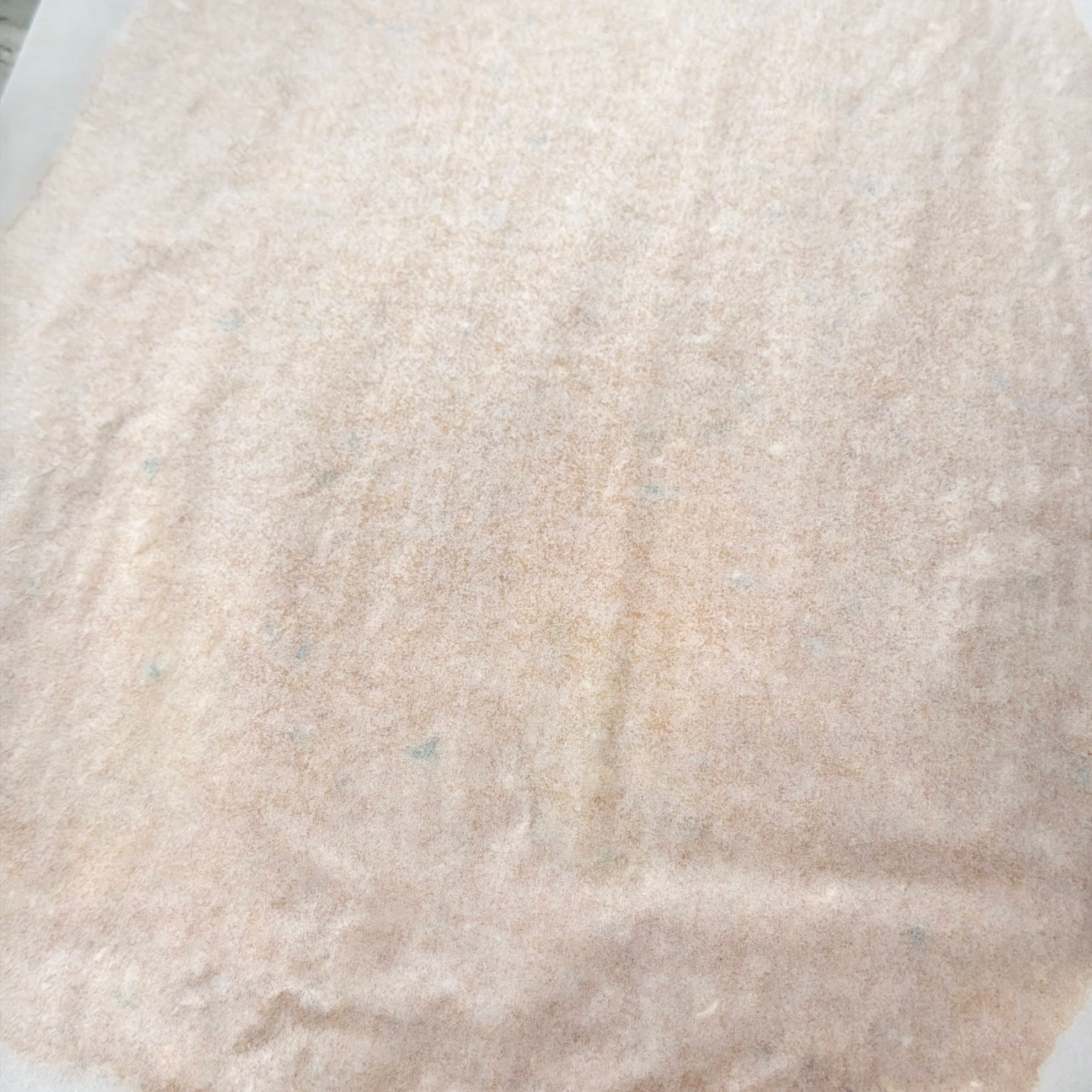 A close-up image of a thin, beige sheet of parchment paper with faint creases and subtle color variations.