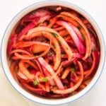 A white bowl filled with sliced red onions and herbs, mixed with a red seasoning or dressing.