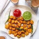 A plate of Moong Dal Pakodas with two dipping sauces (red and green), garnished with green chilies, served alongside cups of tea.