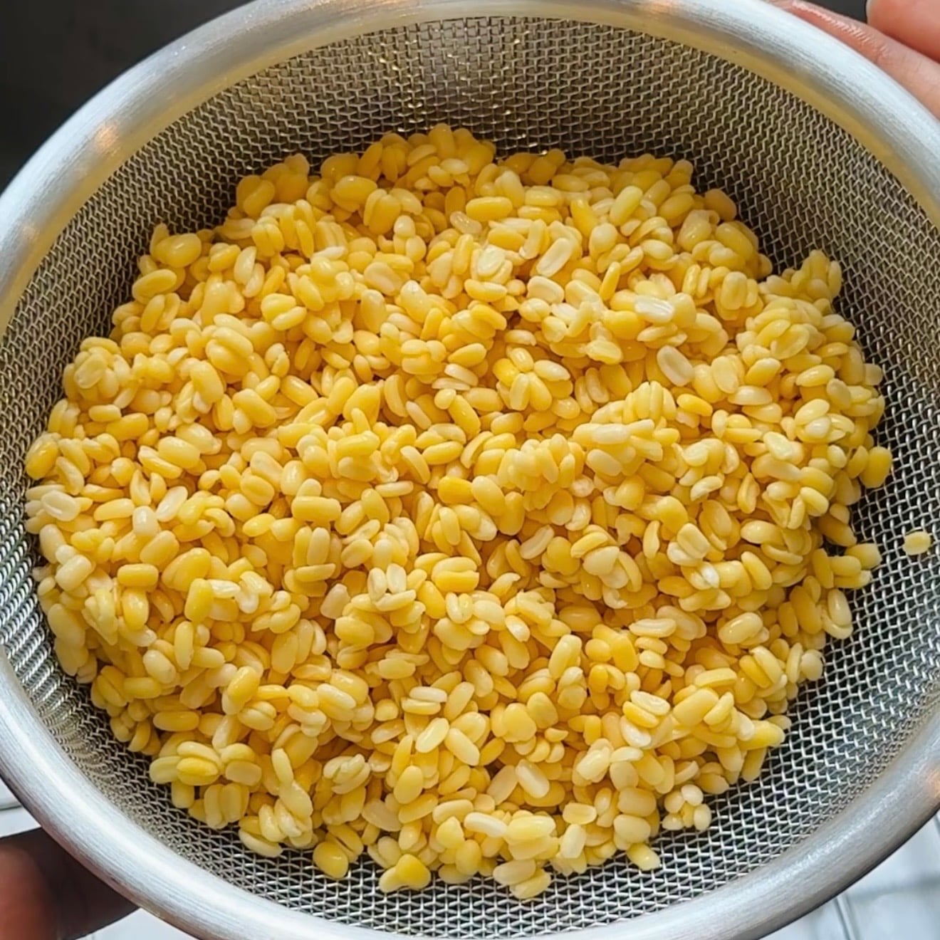 A metal strainer filled with soaked yellow split lentils.