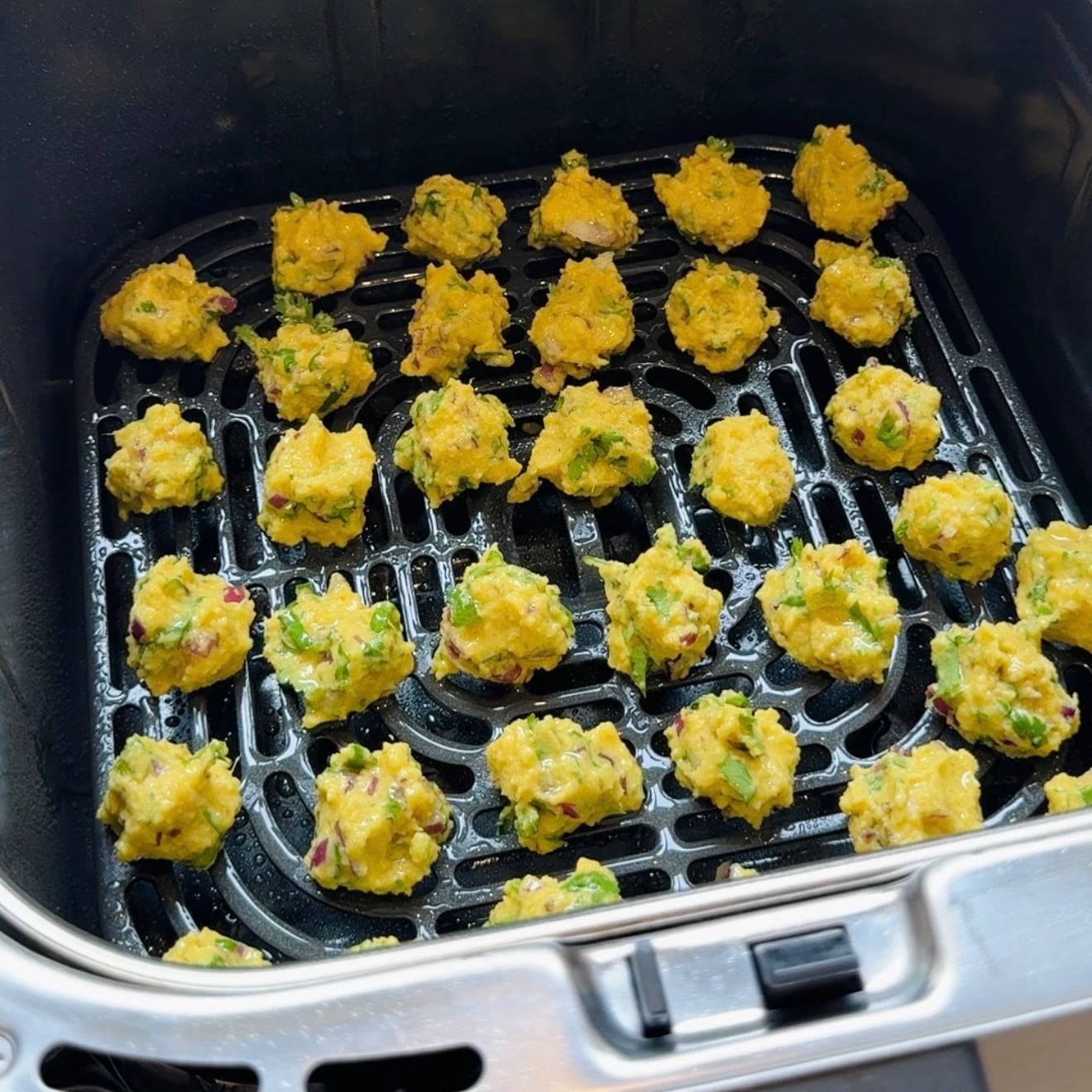 Small yellow vegetable fritter balls arranged in rows inside an air fryer basket, ready to be cooked.
