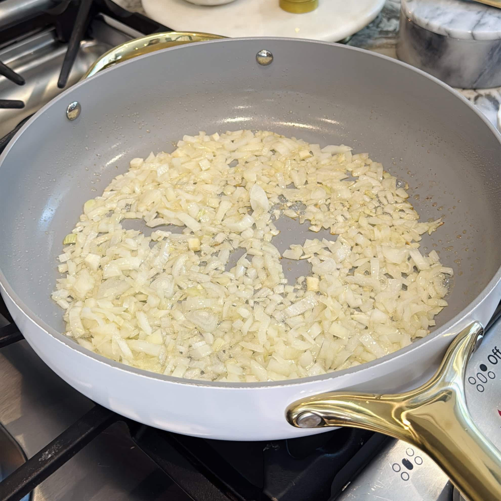 Chopped onions being sautéed in a white frying pan on a stove.