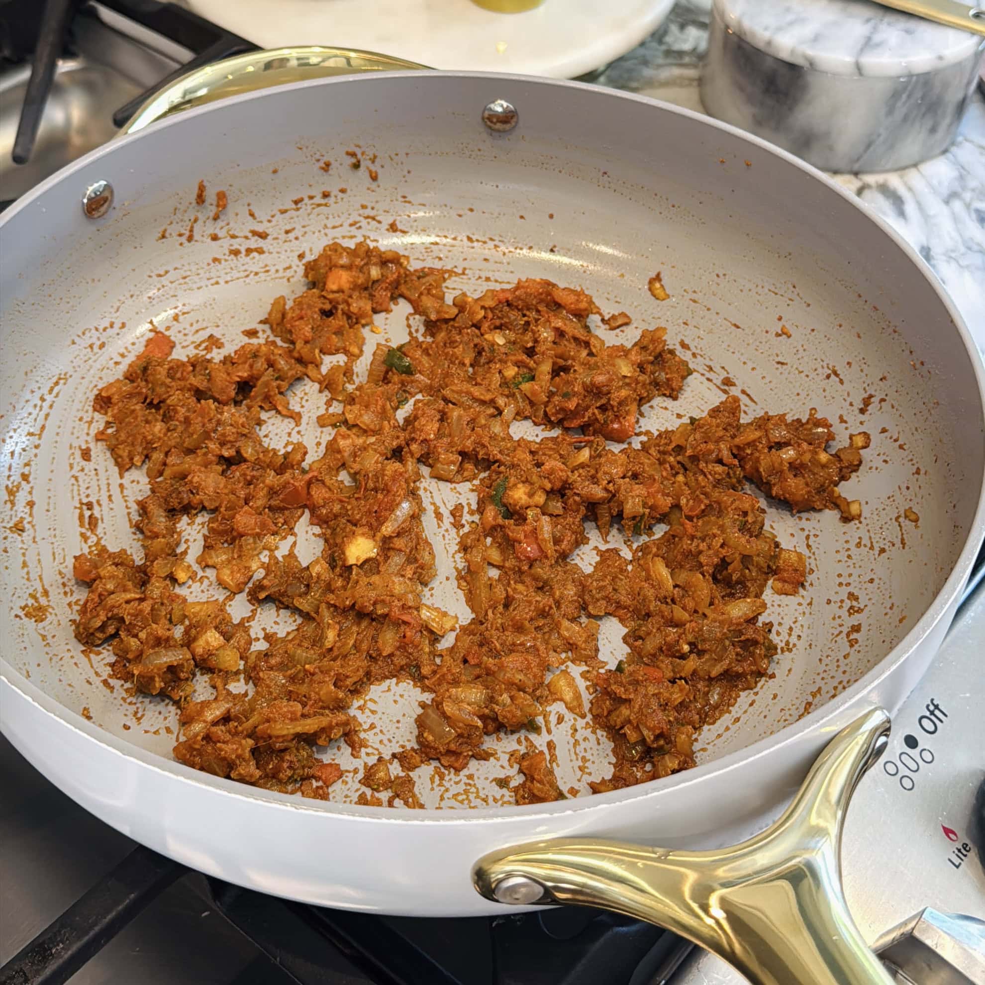 A nonstick pan on a stove contains sautéed onions, spices, and tomatoes being cooked down.