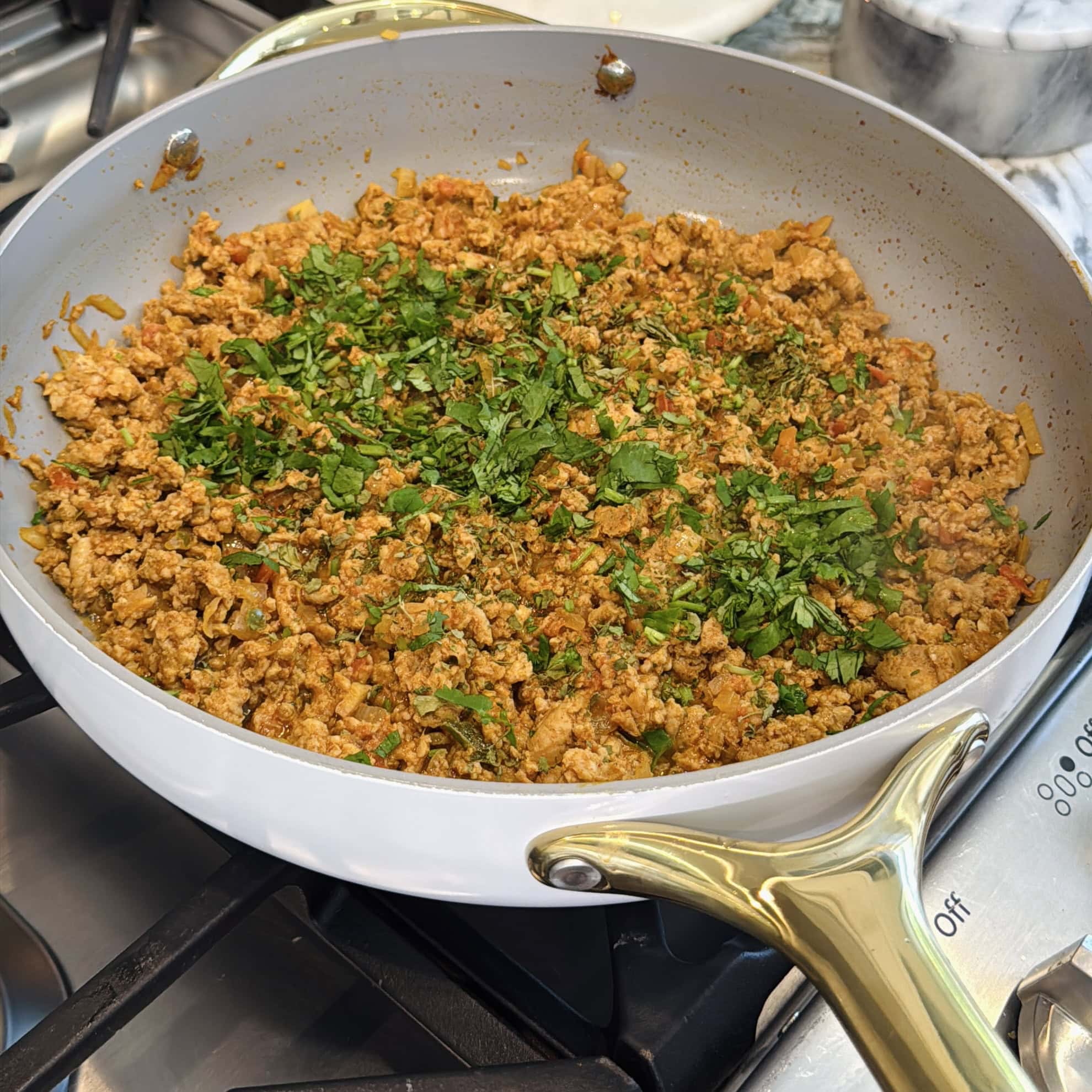 A pan filled with cooked keema, topped with chopped fresh herbs, sits on a stovetop.