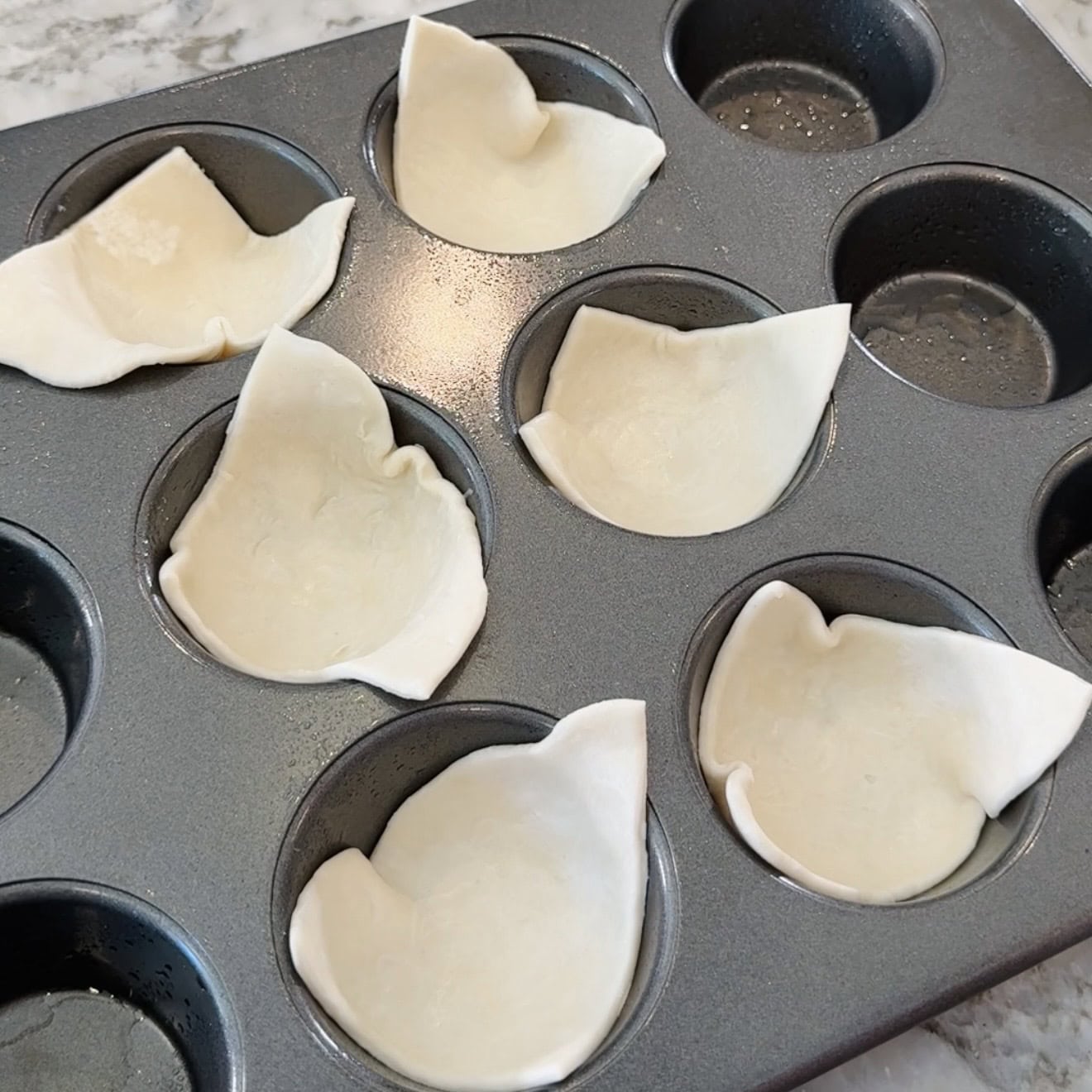 Muffin tin with puff pastry sheets pressed into several of the cups, ready to be filled and baked.