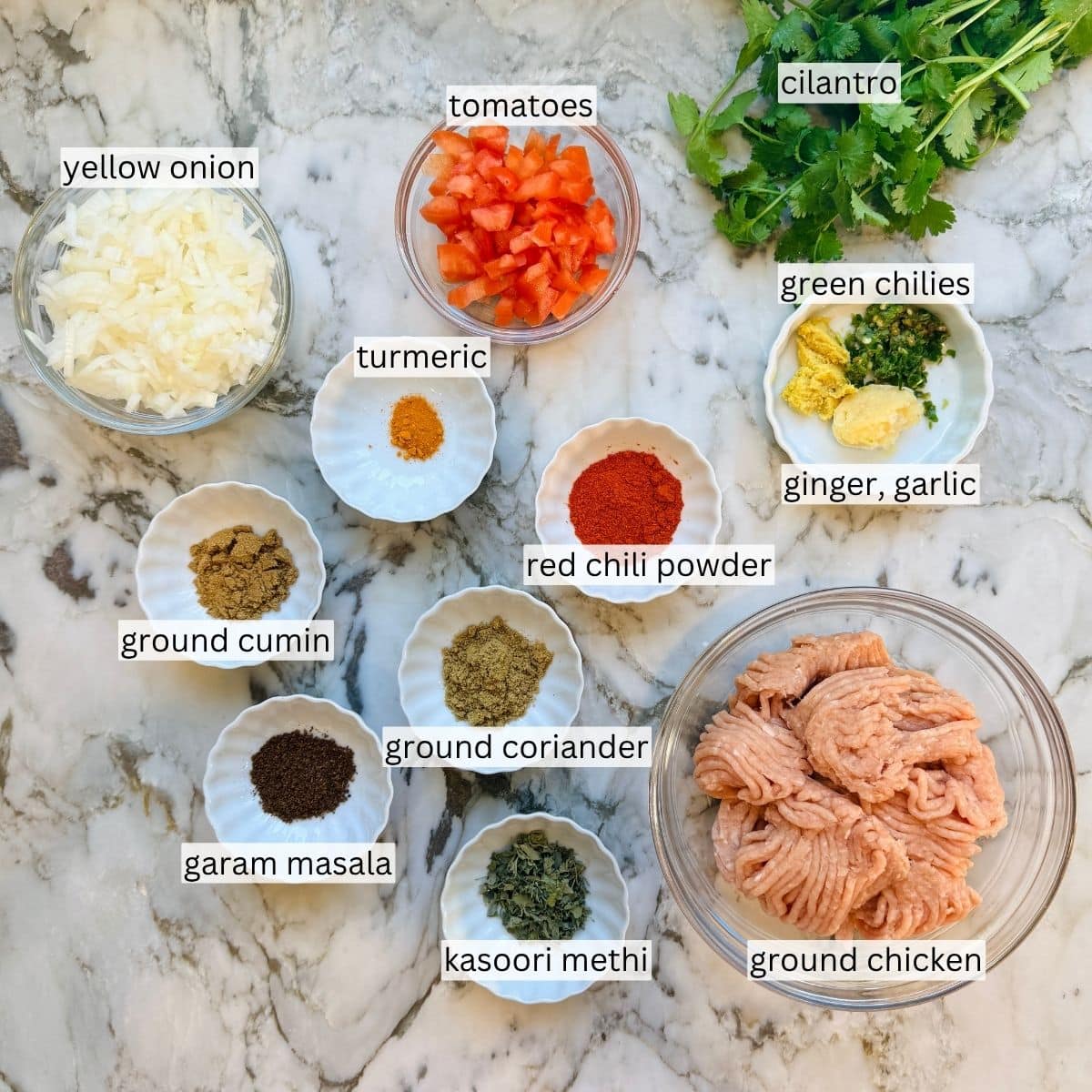ingredients for a chicken keema bites arranged on a marble surface, including ground chicken, spices, chopped vegetables, and herbs.