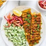 A plate with vegetarian kebabs, chopped cucumber salad, pickled onions, and a lemon wedge, with a small bowl of pickled onions in the background. Text reads Vegetarian Sheet Pan Kebabs.
