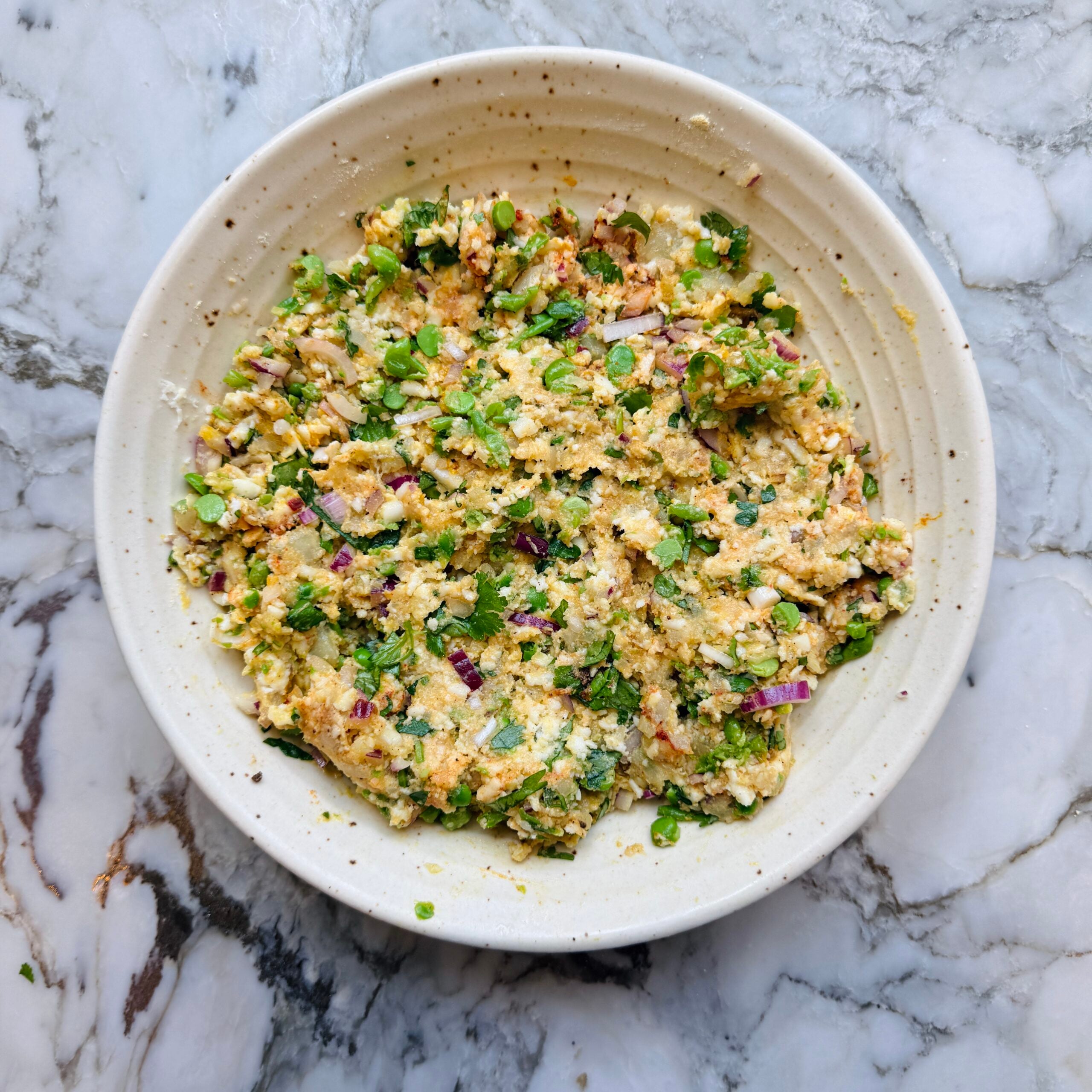 A ceramic bowl filled with a mixed, chunky paneer, potato and spice mixture.