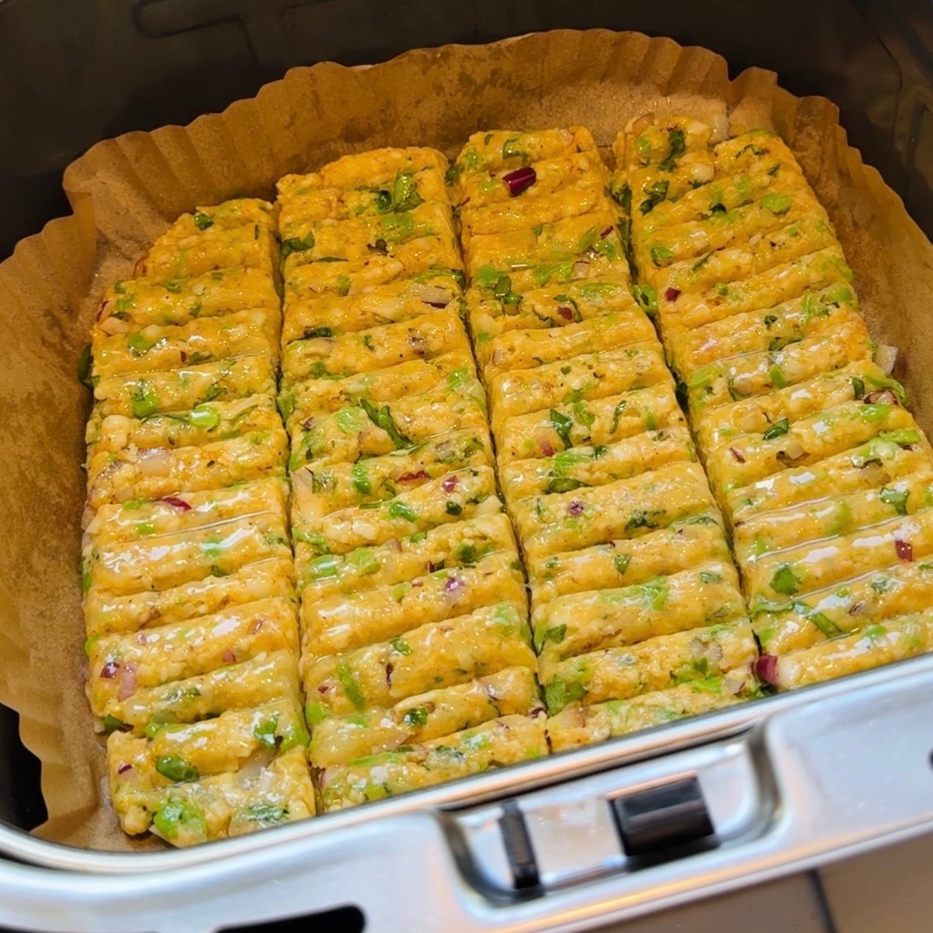 Uncooked vegetable seekh kebabs arranged in rows on parchment paper inside an air fryer basket.