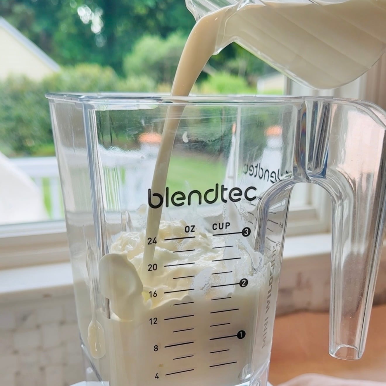 Milk is being poured into a Blendtec blender jar filled with yogurt and ice.