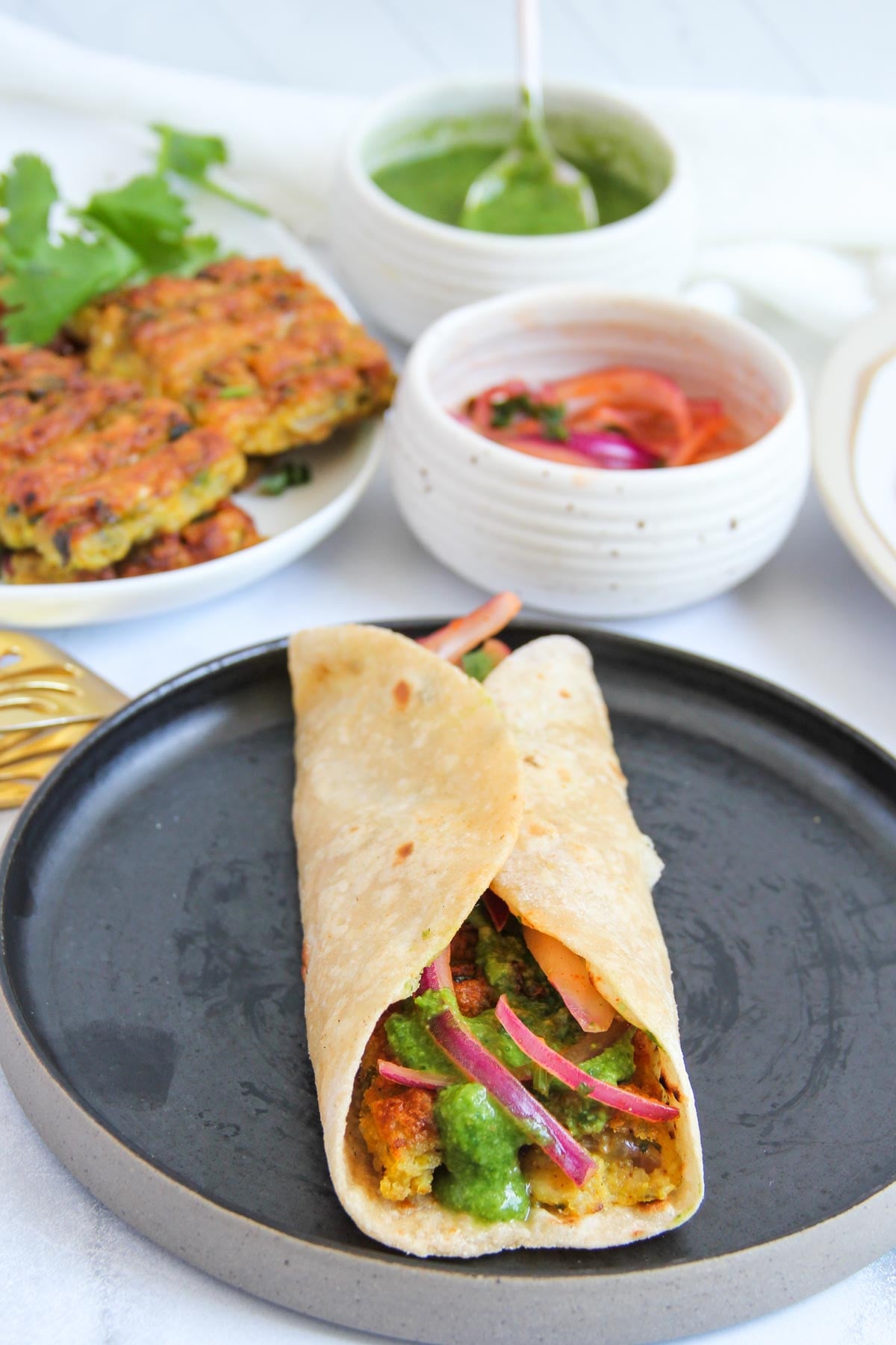 A rolled flatbread wrap filled with vegetarian kebab, green chutney, and pickled onions on a black plate.
