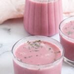 Three clear glasses filled with pink sol kadhi, garnished with herbs, are placed on a light surface. A jug of sol kadhi sits in the background. Text on the image describes the recipe.