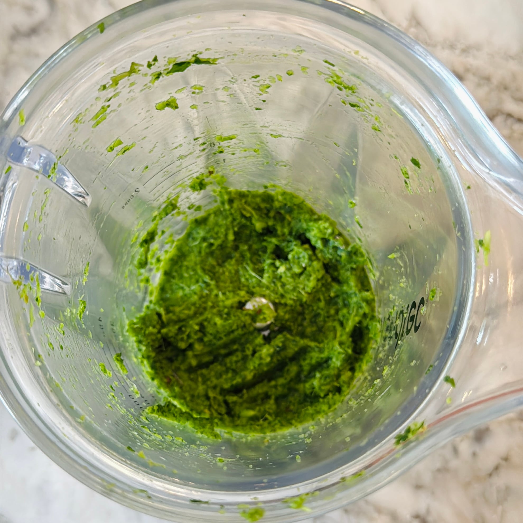 Top view of a blender containing a thick, green paste mixture on a marble countertop.
