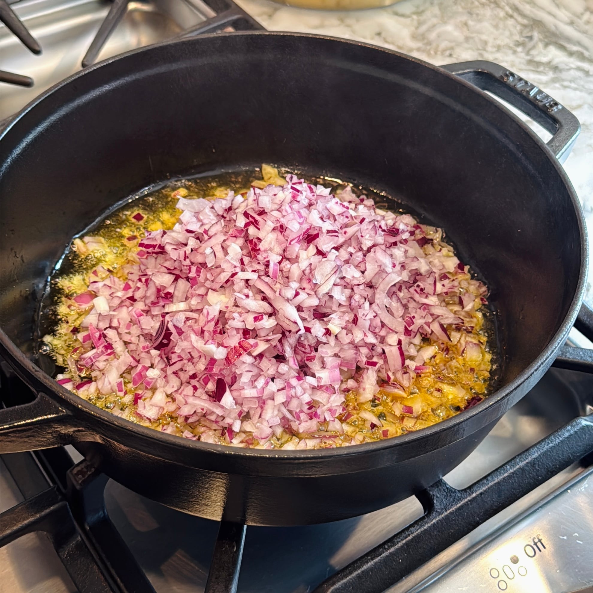 Chopped red onions are sautéing in oil in a black cast iron pot on a gas stove.