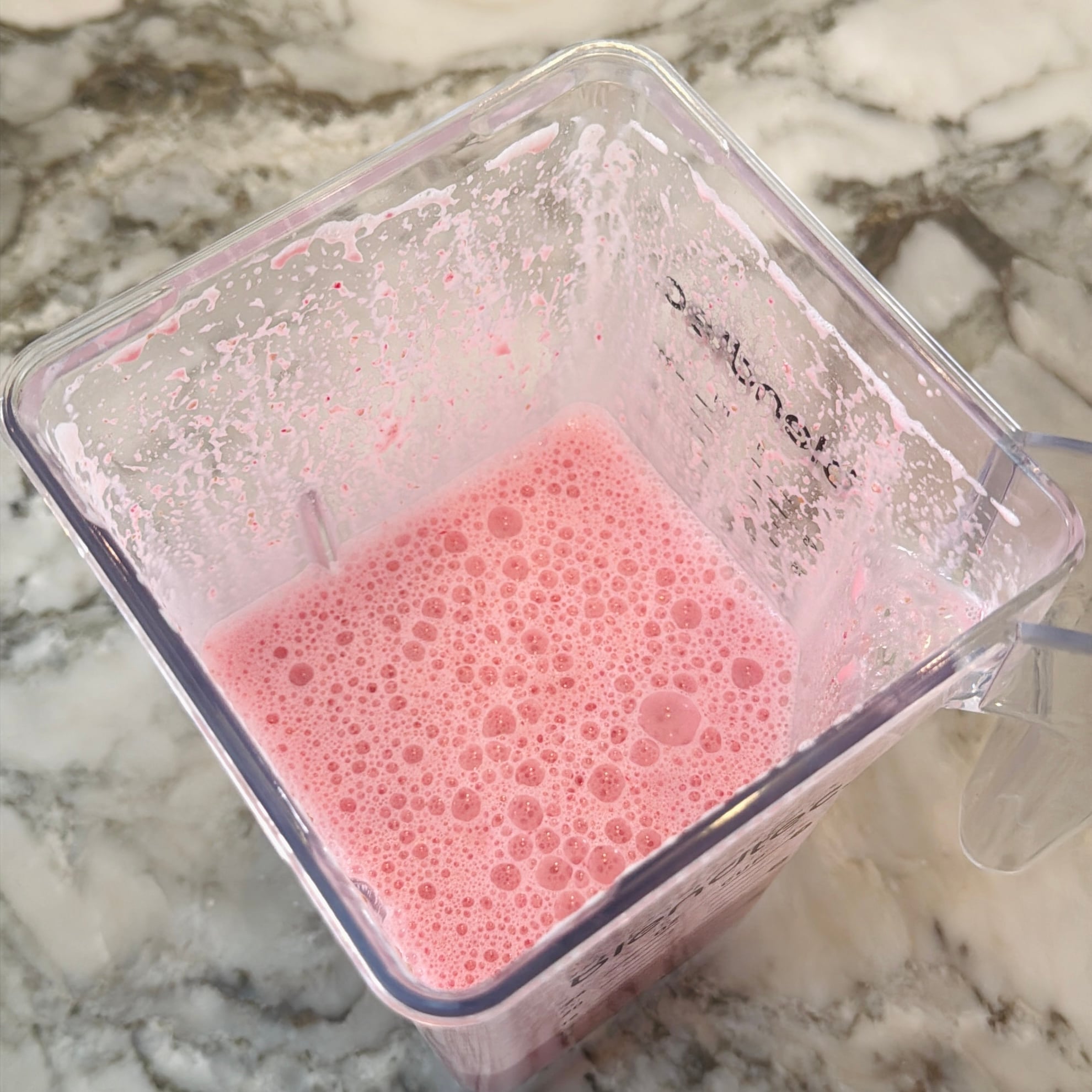 A blender container with pink solkadhi on a marble countertop.