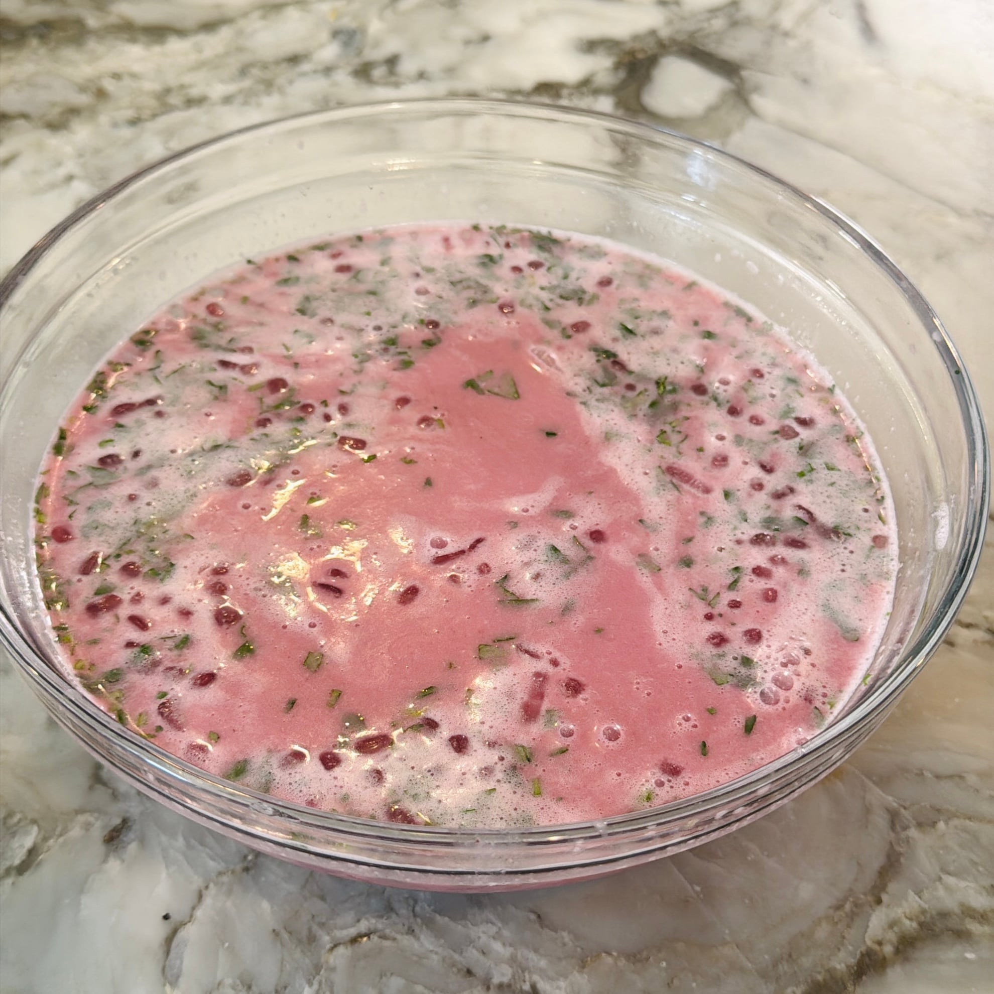 A glass bowl filled with a pink, frothy solkadhi with chopped cilantro.