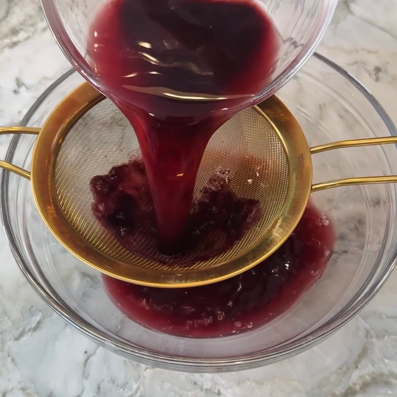 kokum extract poured through a fine mesh strainer into a clear glass bowl, separating solids from the juice.