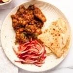 A plate with chicken sukka, sliced red onions , and roti.
