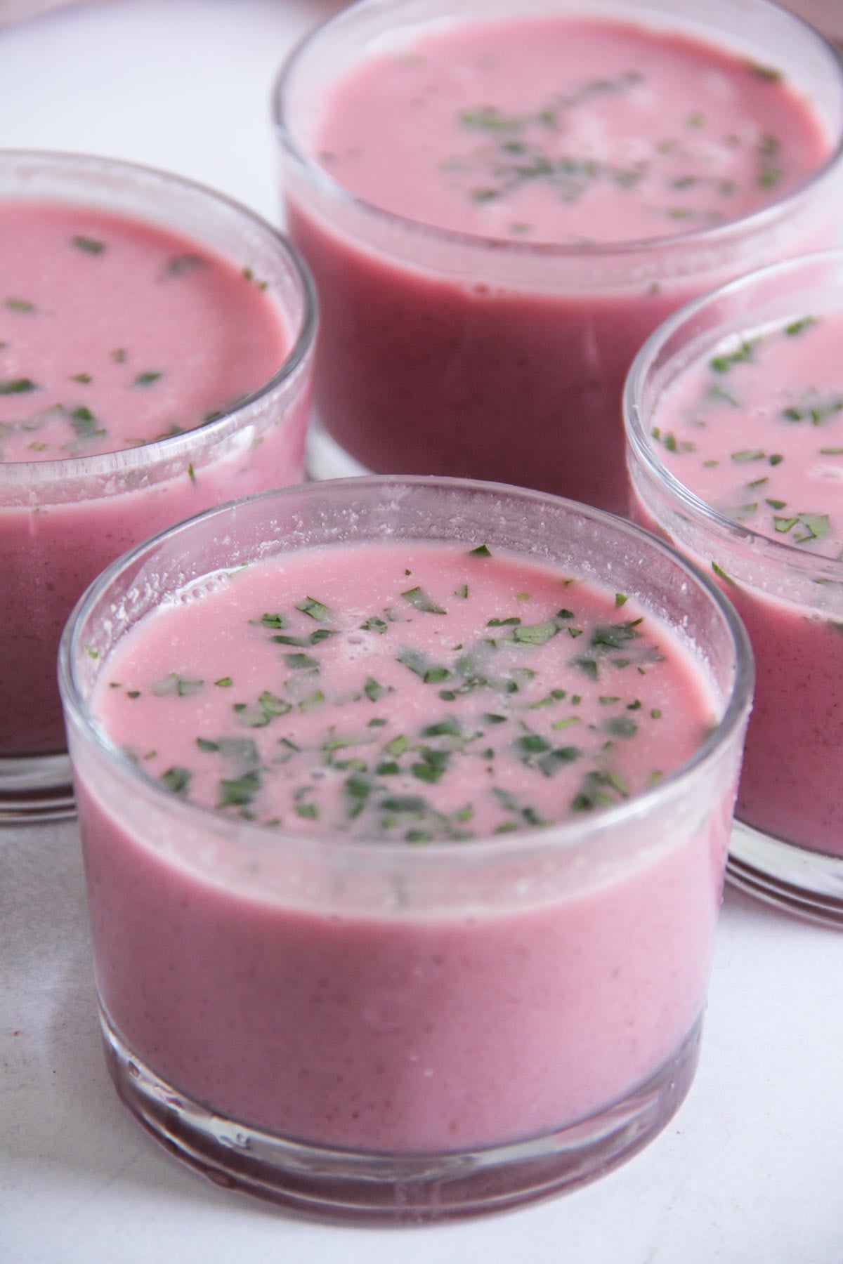 Four glass cups filled with pink solkadhi topped with finely chopped cilantro.