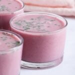 A close-up of glass cups filled with pink solkadhi, garnished with cilantro.