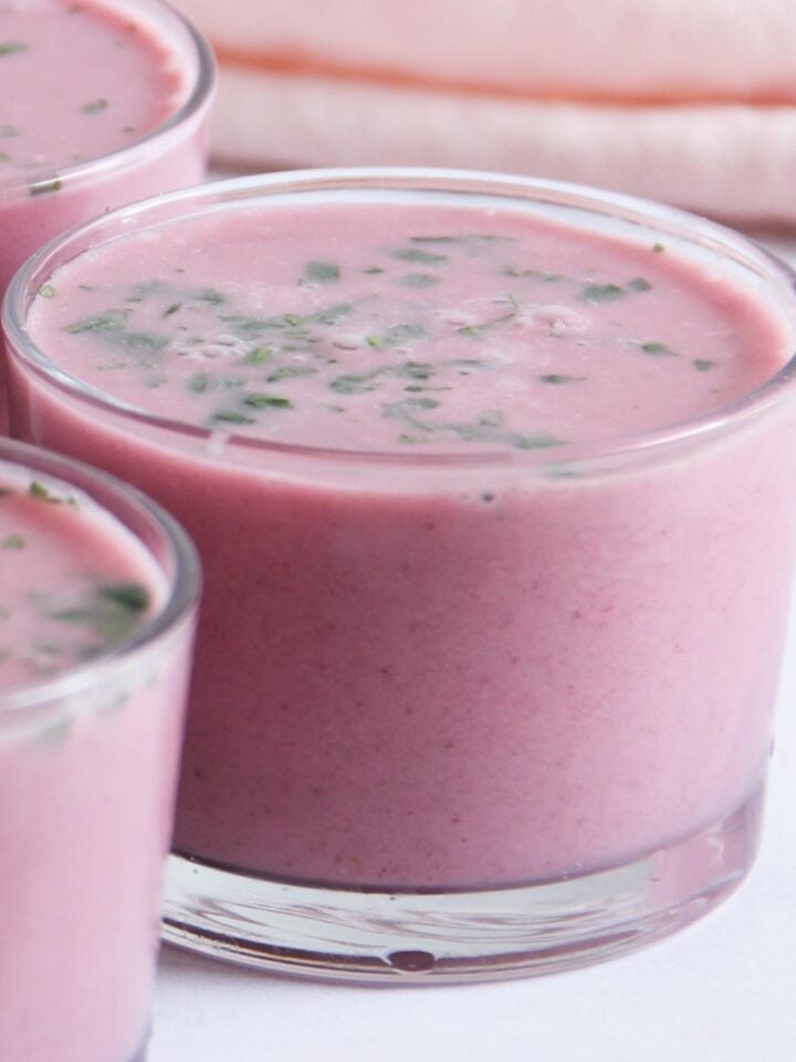 A close-up of glass cups filled with pink solkadhi, garnished with cilantro.