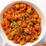 A white bowl filled with Sandgyachi Bhaji (Maharashtrian vade curry) garnished with chopped herbs, next to folded flatbread on a white surface.