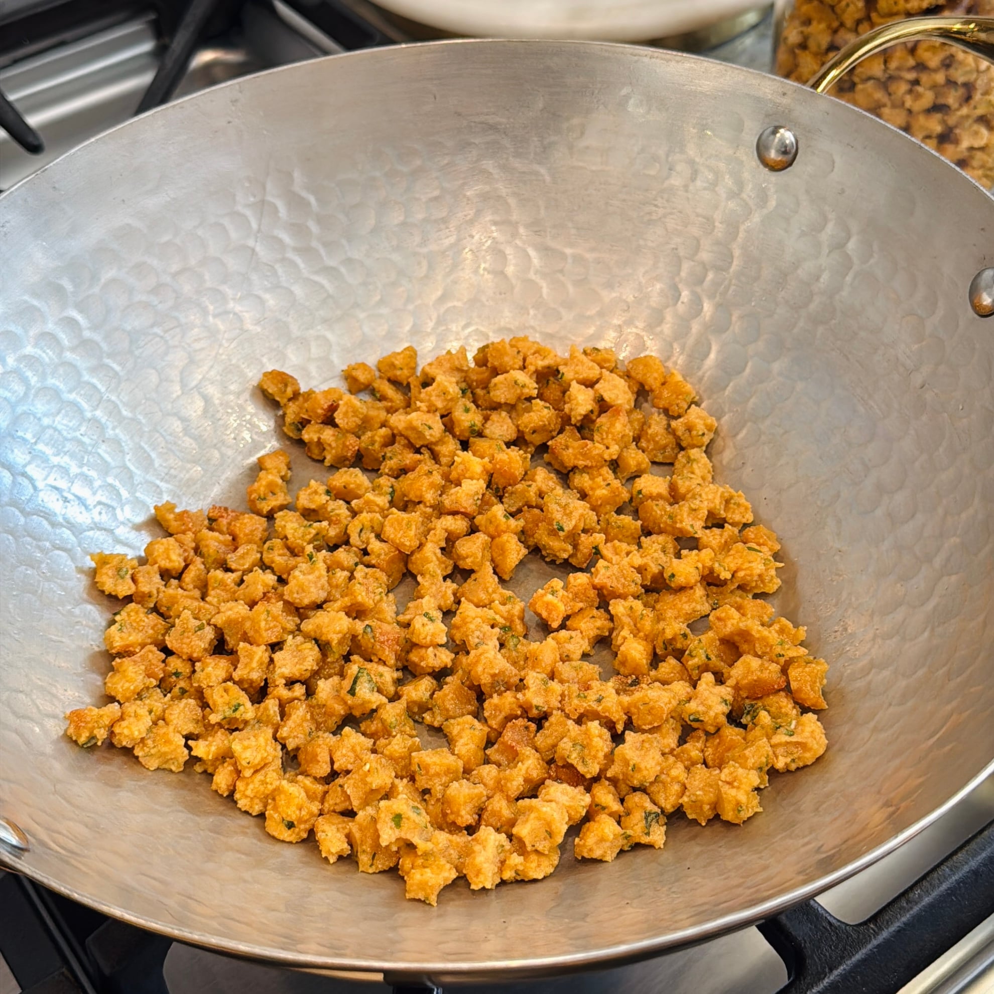 Small golden-brown fried sandge in a kadai on a stove.