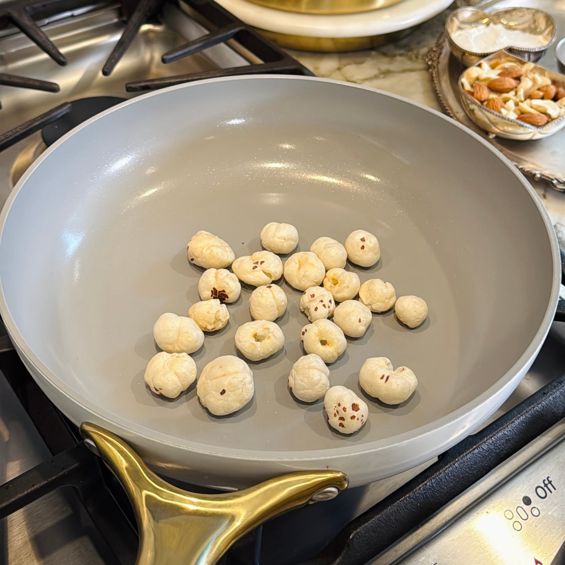 A nonstick pan with fox nuts roasting on a gas stove.