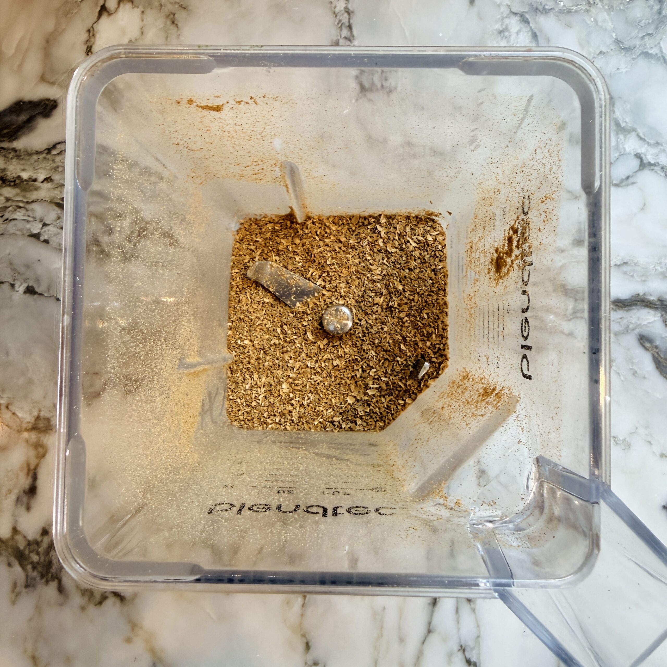 Overhead view of a blender with ground coriander seeds inside.