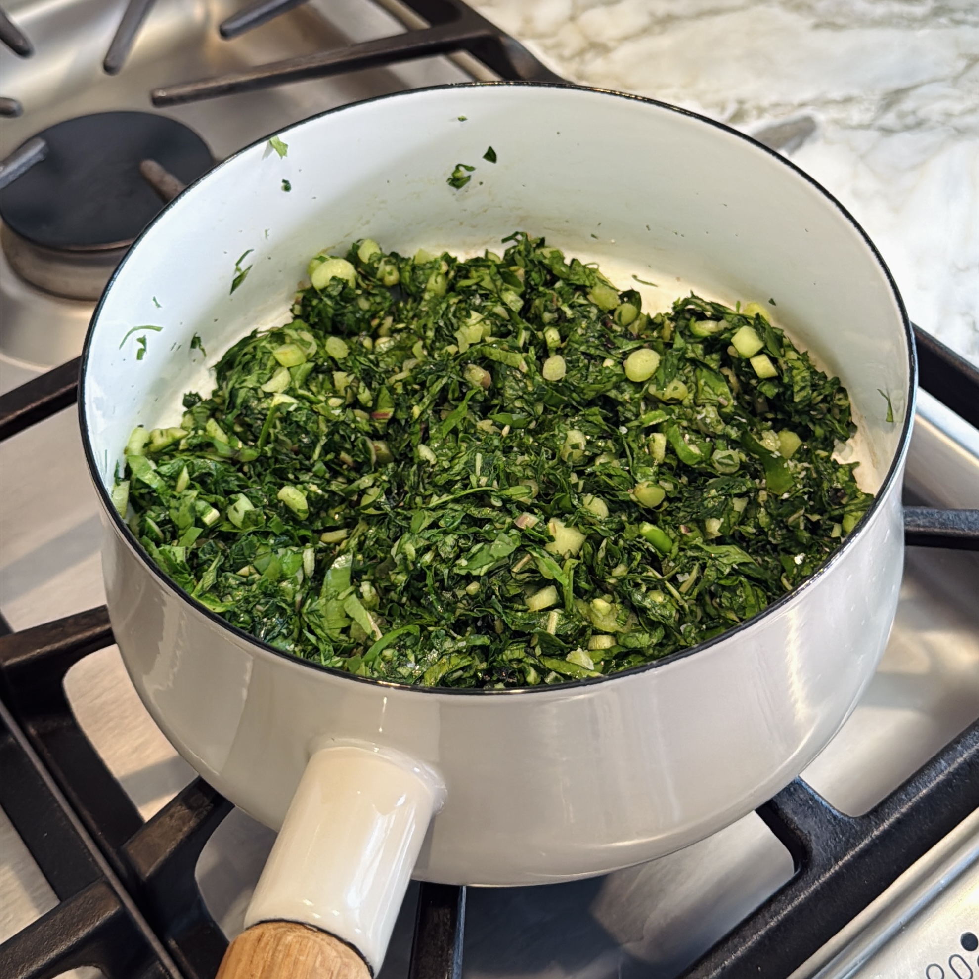 A white pot on a stovetop containing sautéed chopped Colocasia greens.