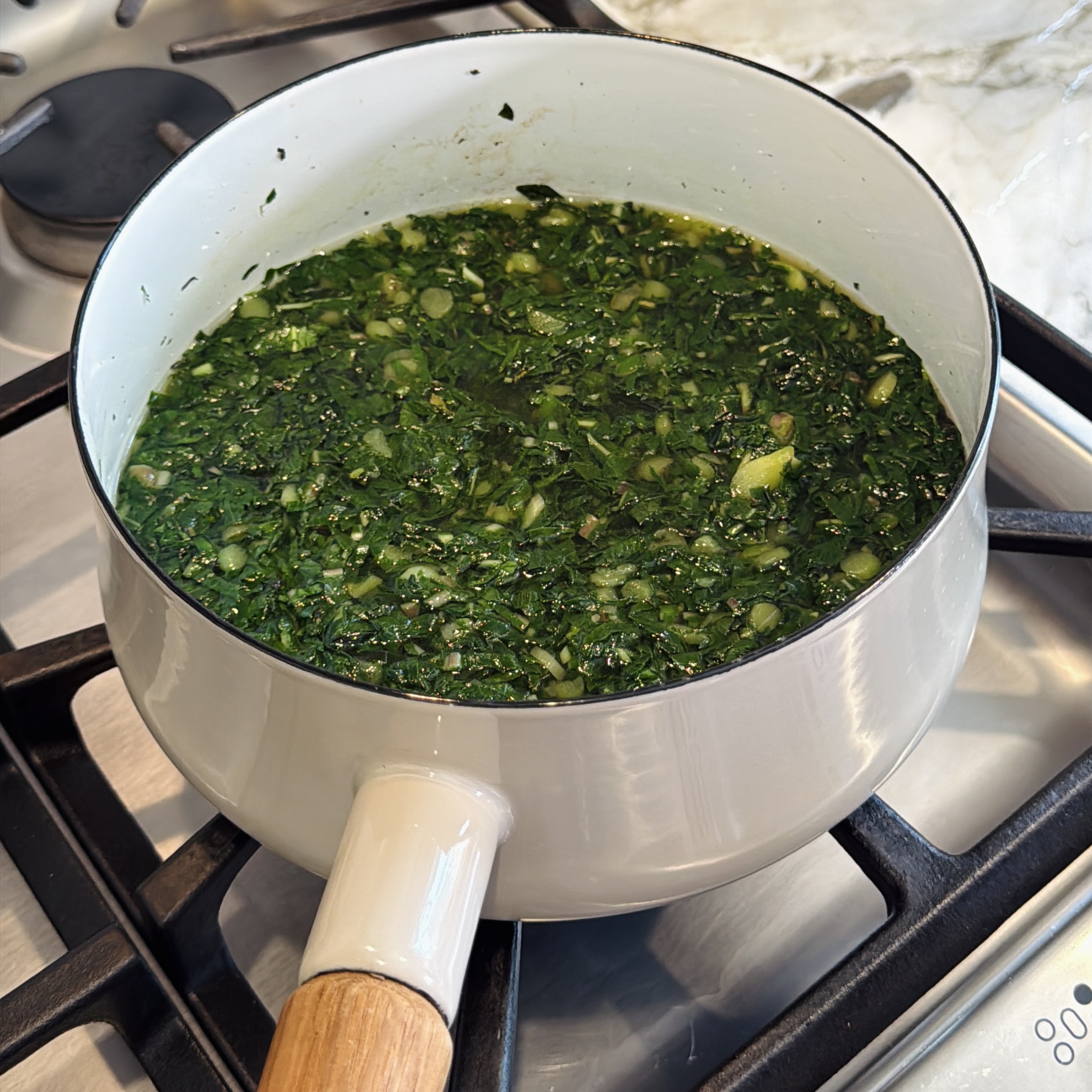 A saucepan on a stovetop with alu greens cooking in hot water.