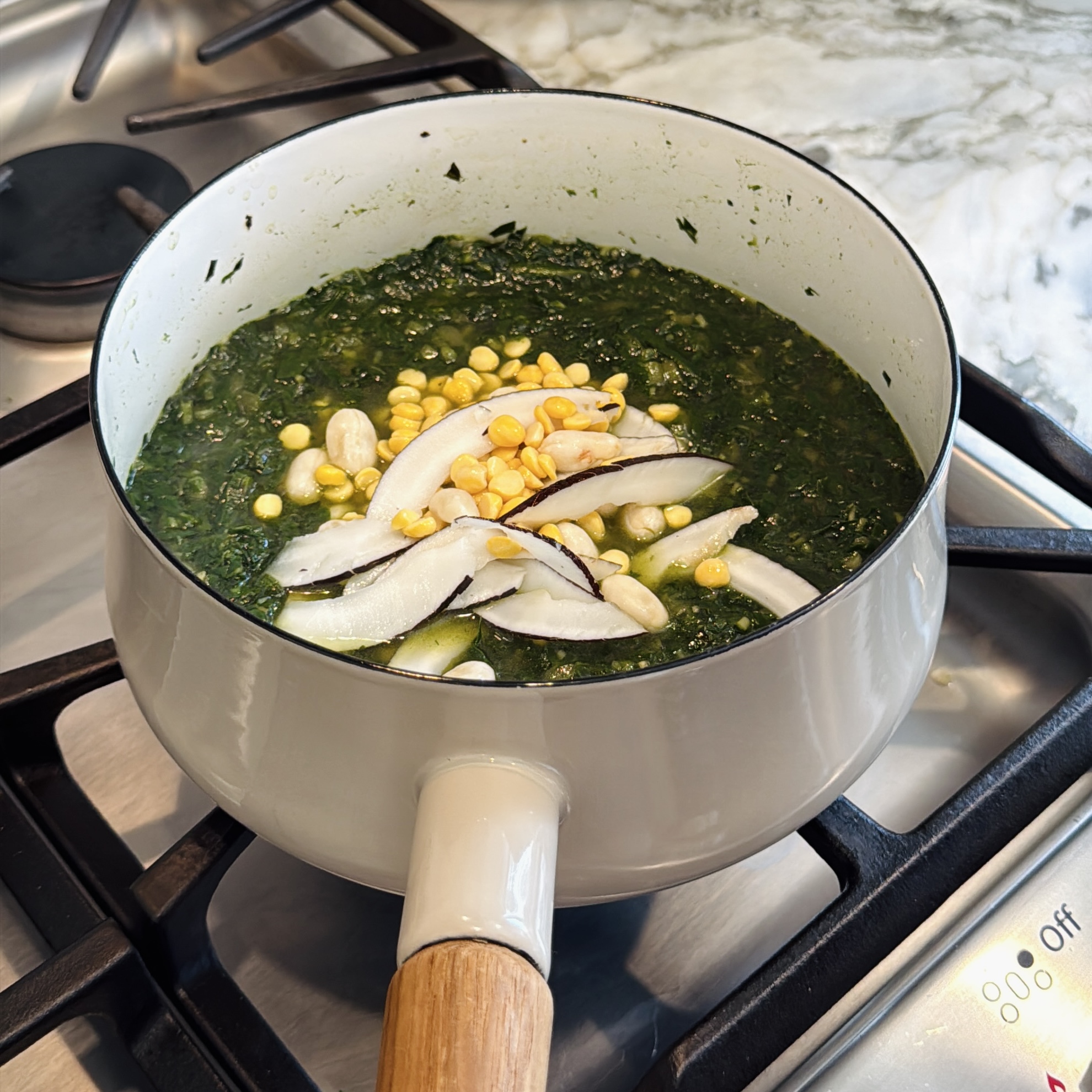 A pot of cooked green leafy vegetables topped with chana dal, peanuts, and slices of coconut on a stovetop.