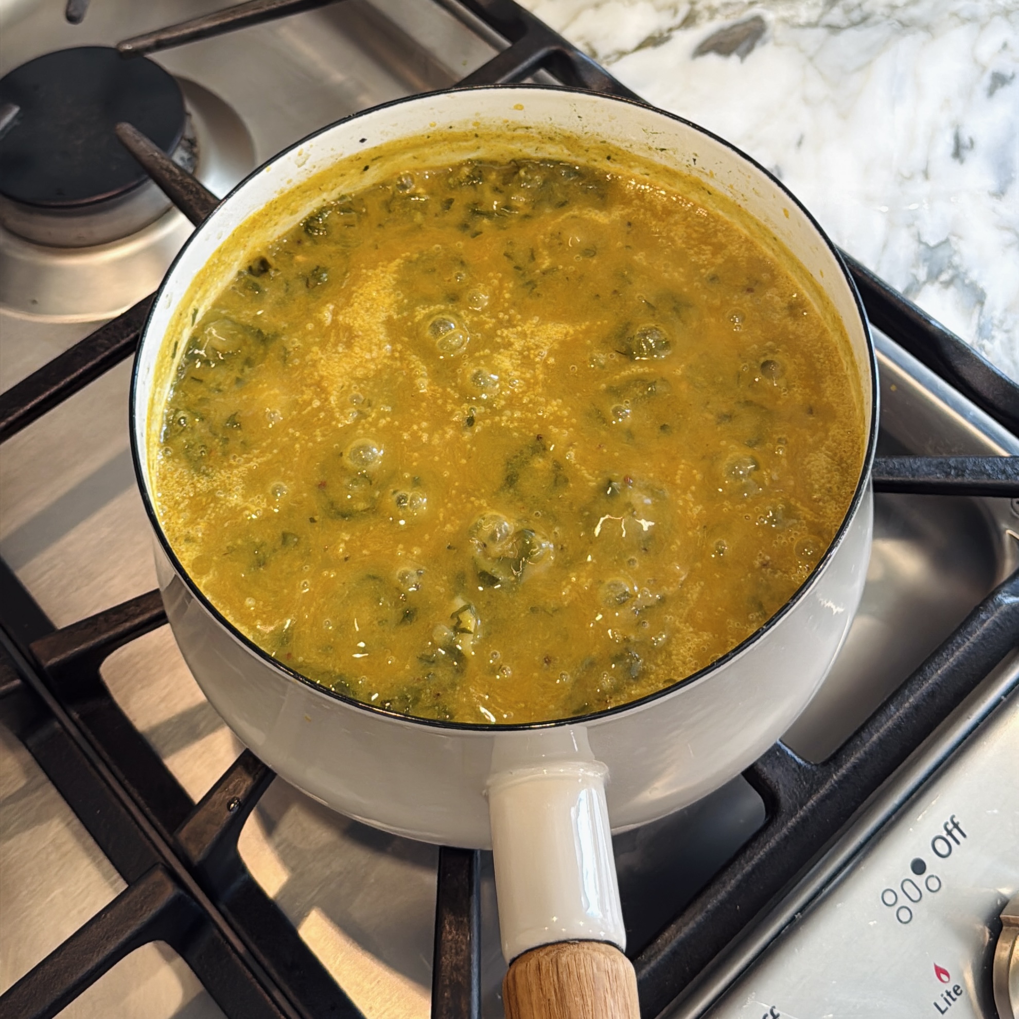 A white pot of alu chi bhaji simmering on a stovetop.