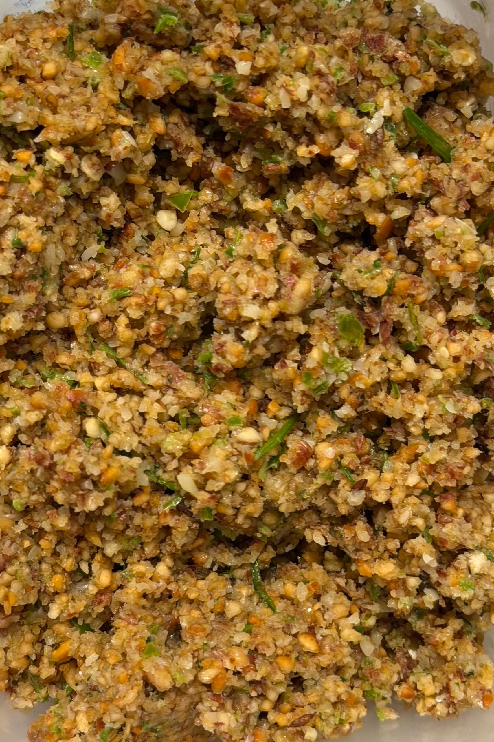 Close-up of a coarse, mixed nut and herb blend with visible pieces of green herbs and nuts throughout.