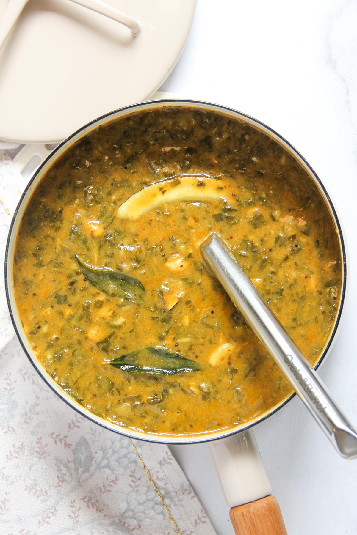 A metal saucepan containing creamy green leafy vegetable curry with a serving spoon inside.