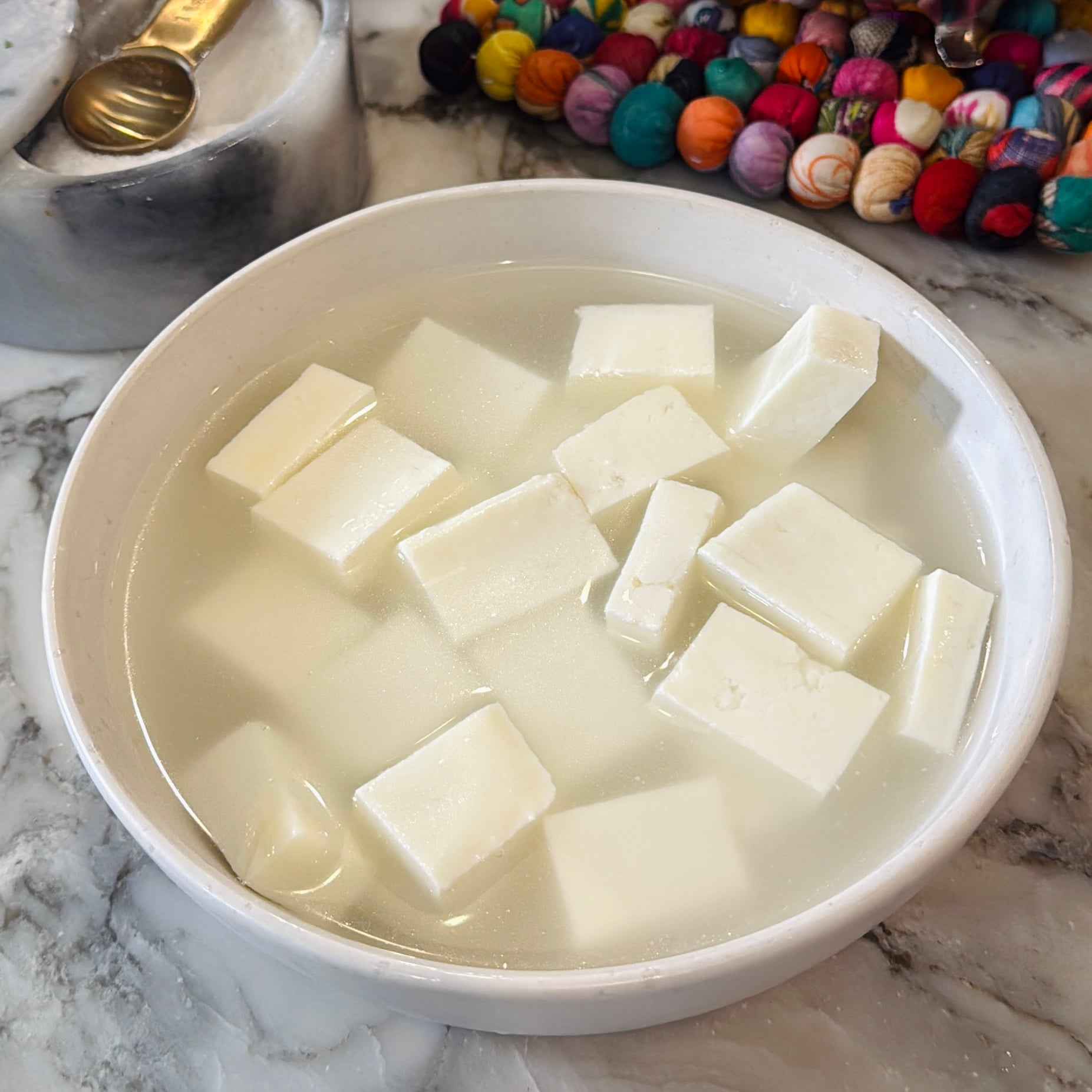 A white bowl containing cubes of white cheese submerged in water.