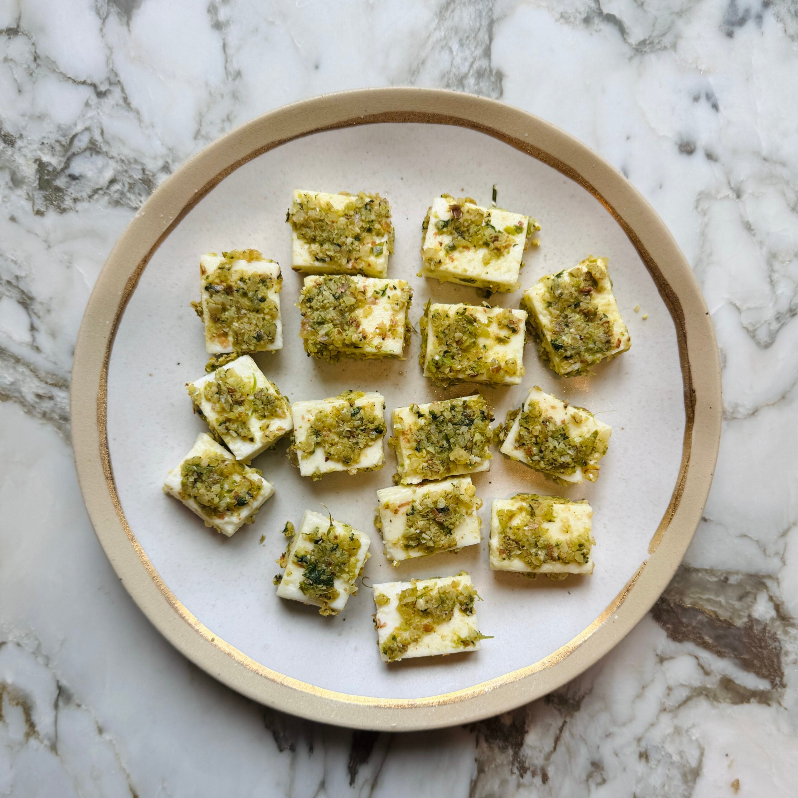 Cubed cheese topped with a green herb mixture on a round plate.
