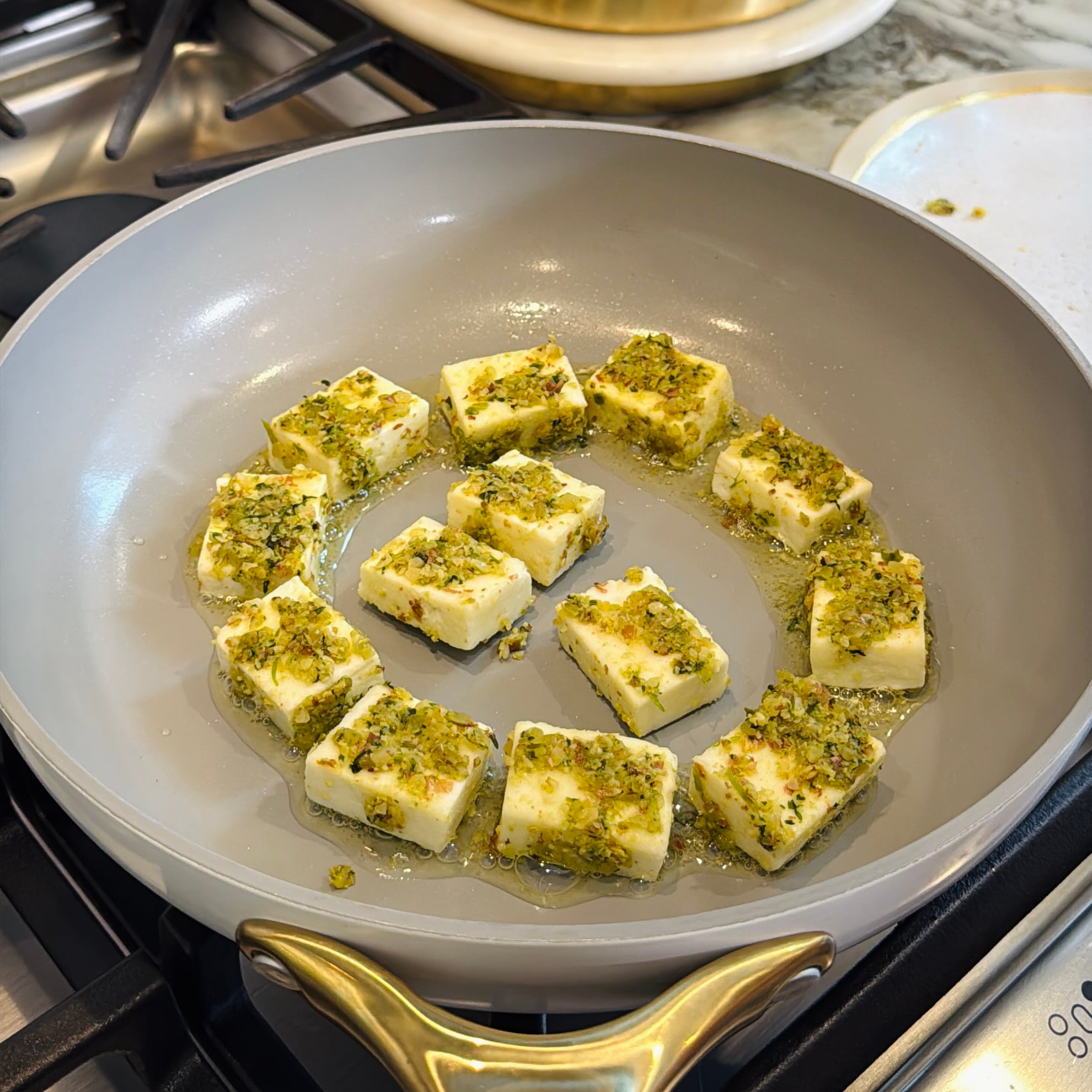Cubed paneer coated in crushed pistachios frying in a pan.
