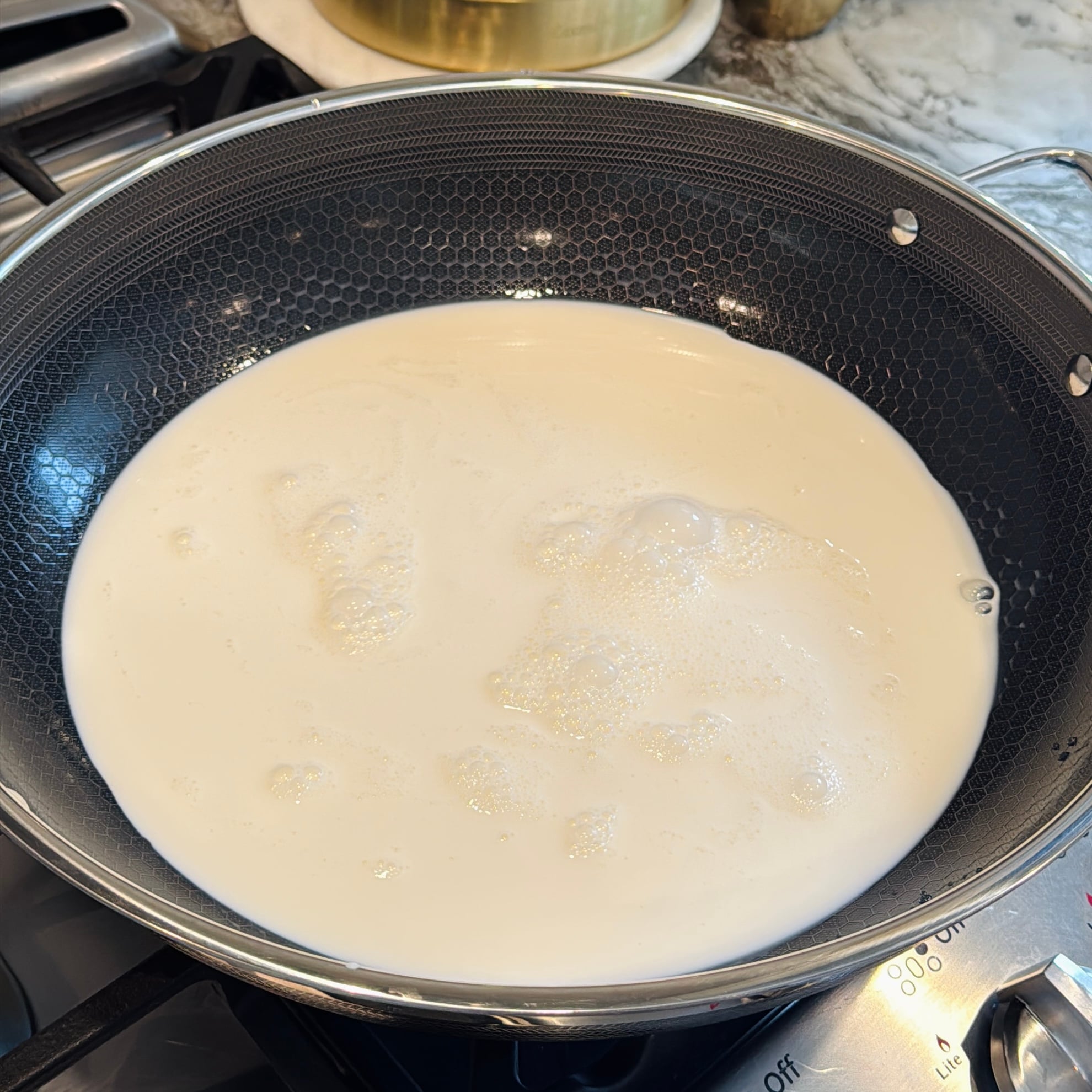 Milk heating in a black, wide kadai on a stovetop.