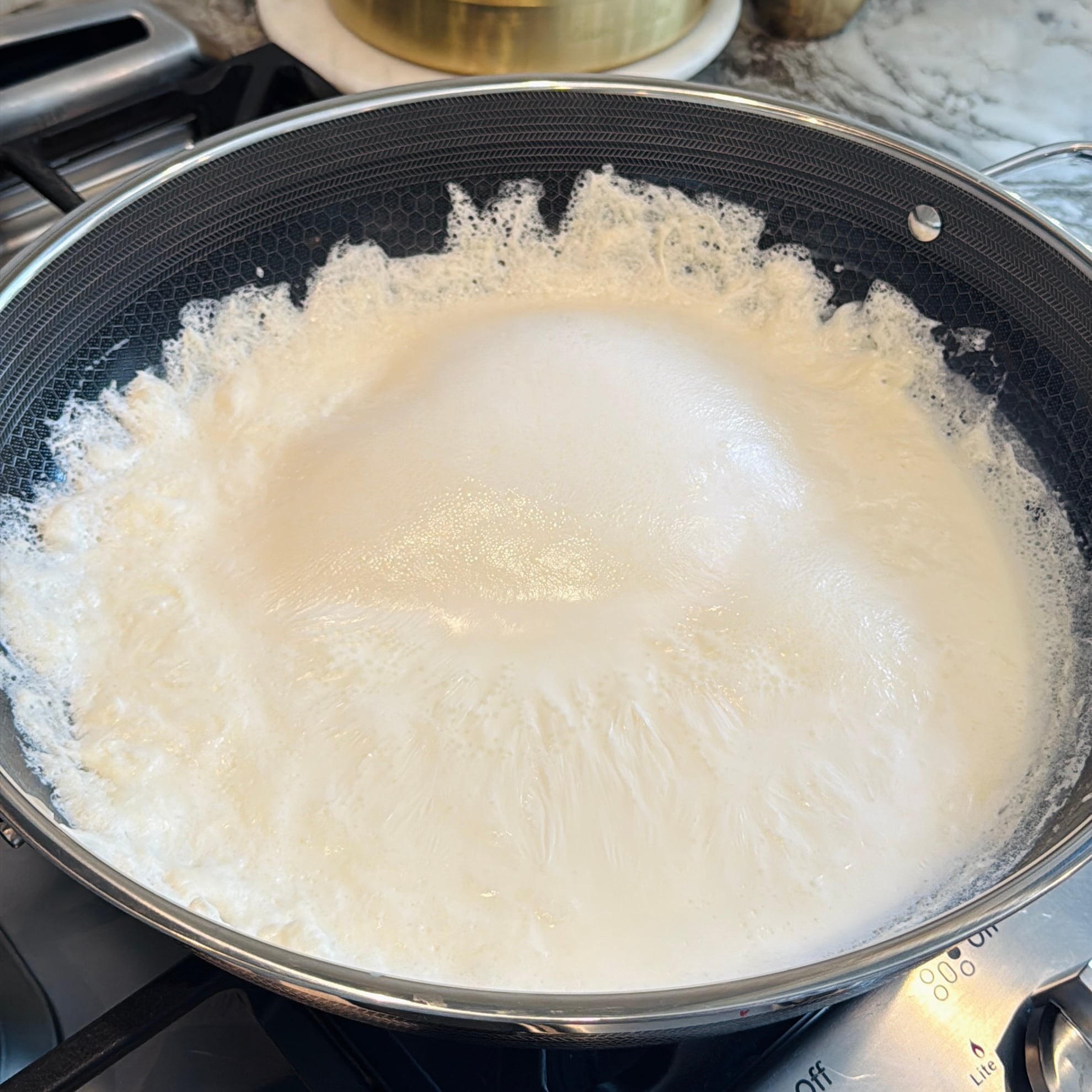Kadai on a stovetop filled with bubbling, foamy milk.