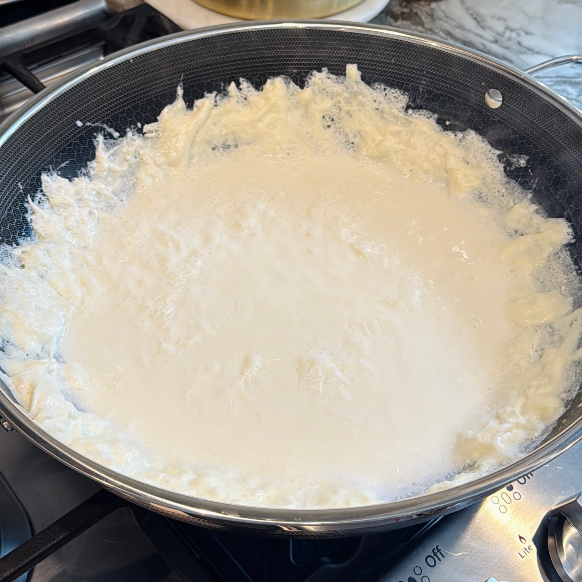 Milk simmering in a wide kadai on stovetop.