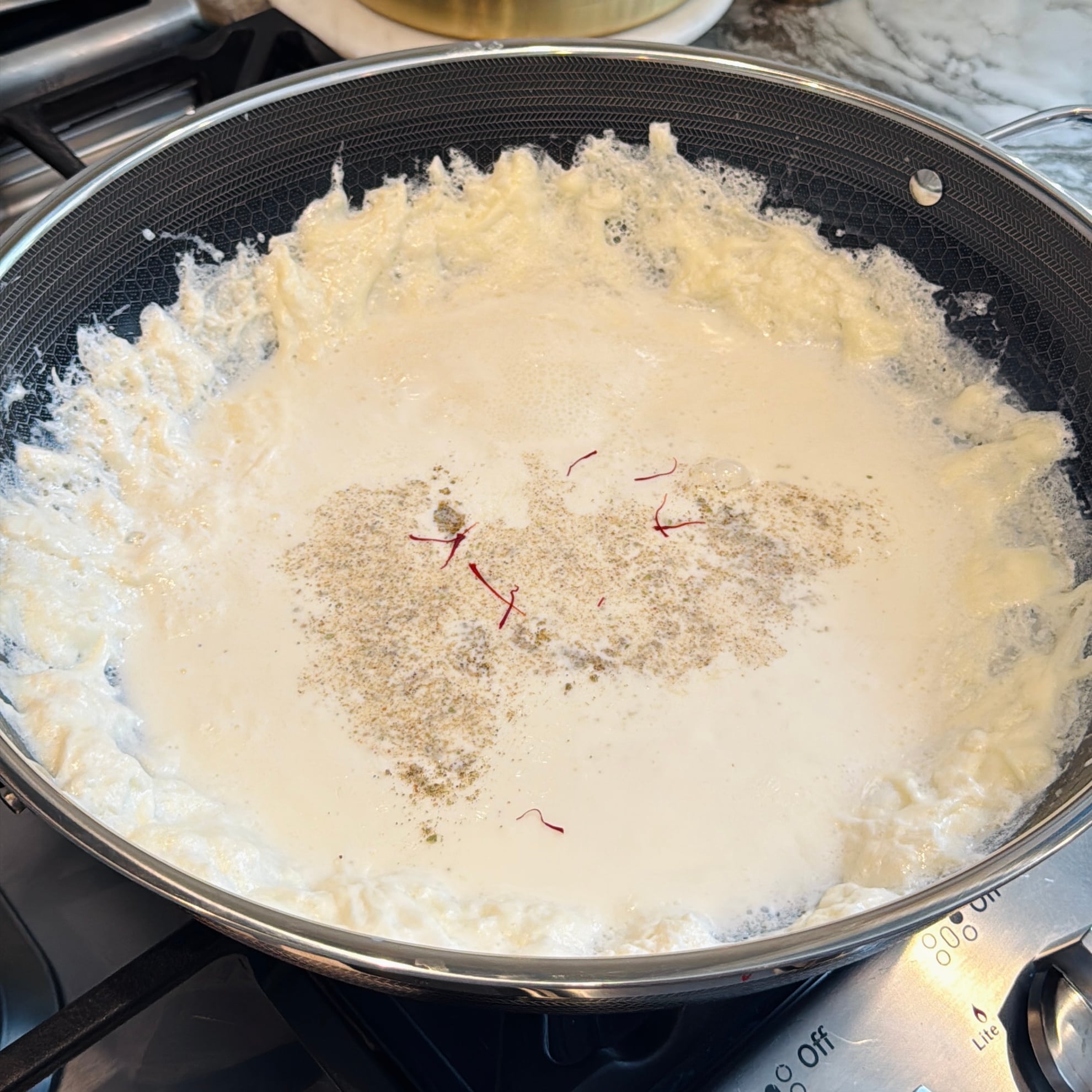 Cream and milk solids simmering in a pan, seasoned with cardamom and saffron threads.