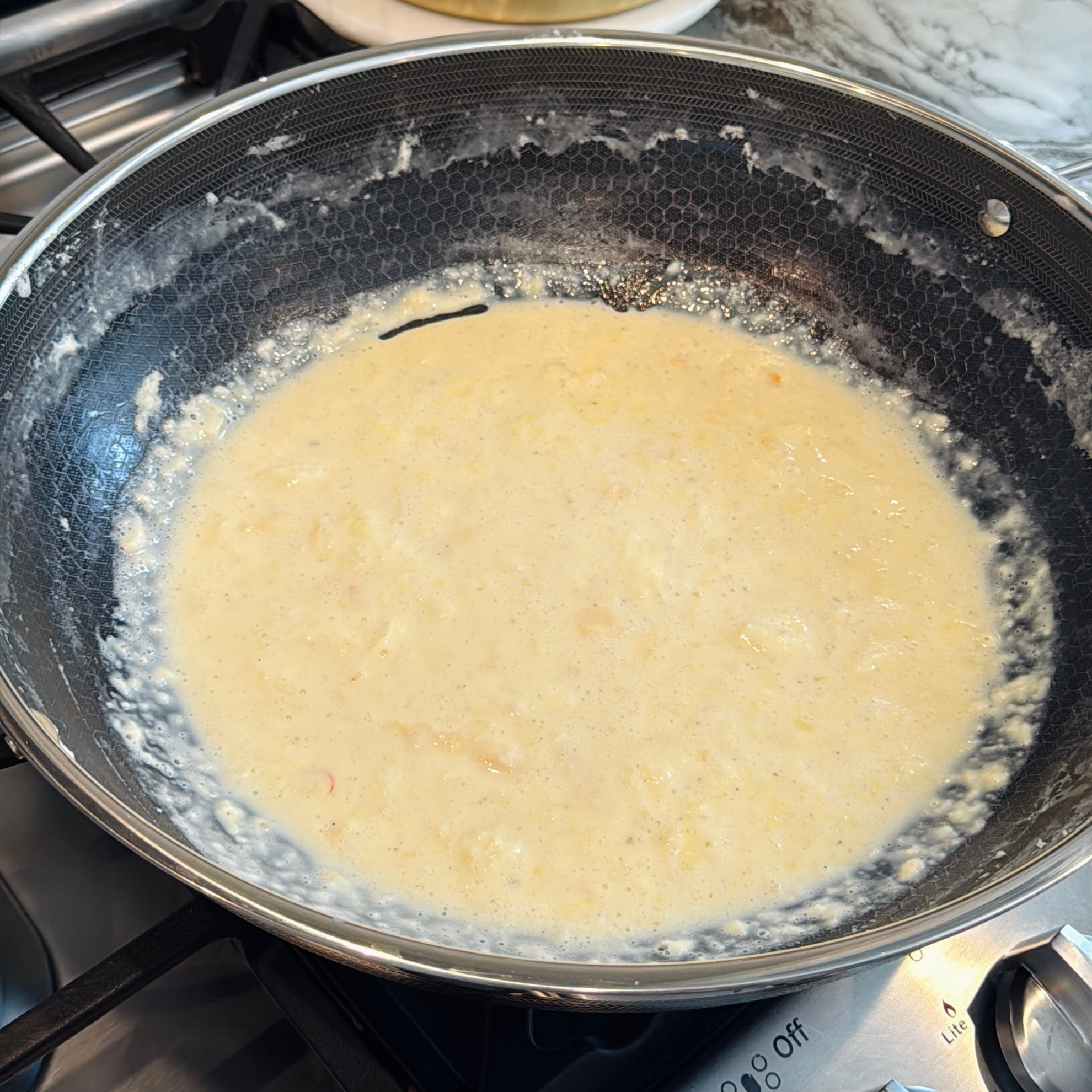 Creamy rabdi simmering in a textured metal skillet on a stovetop.