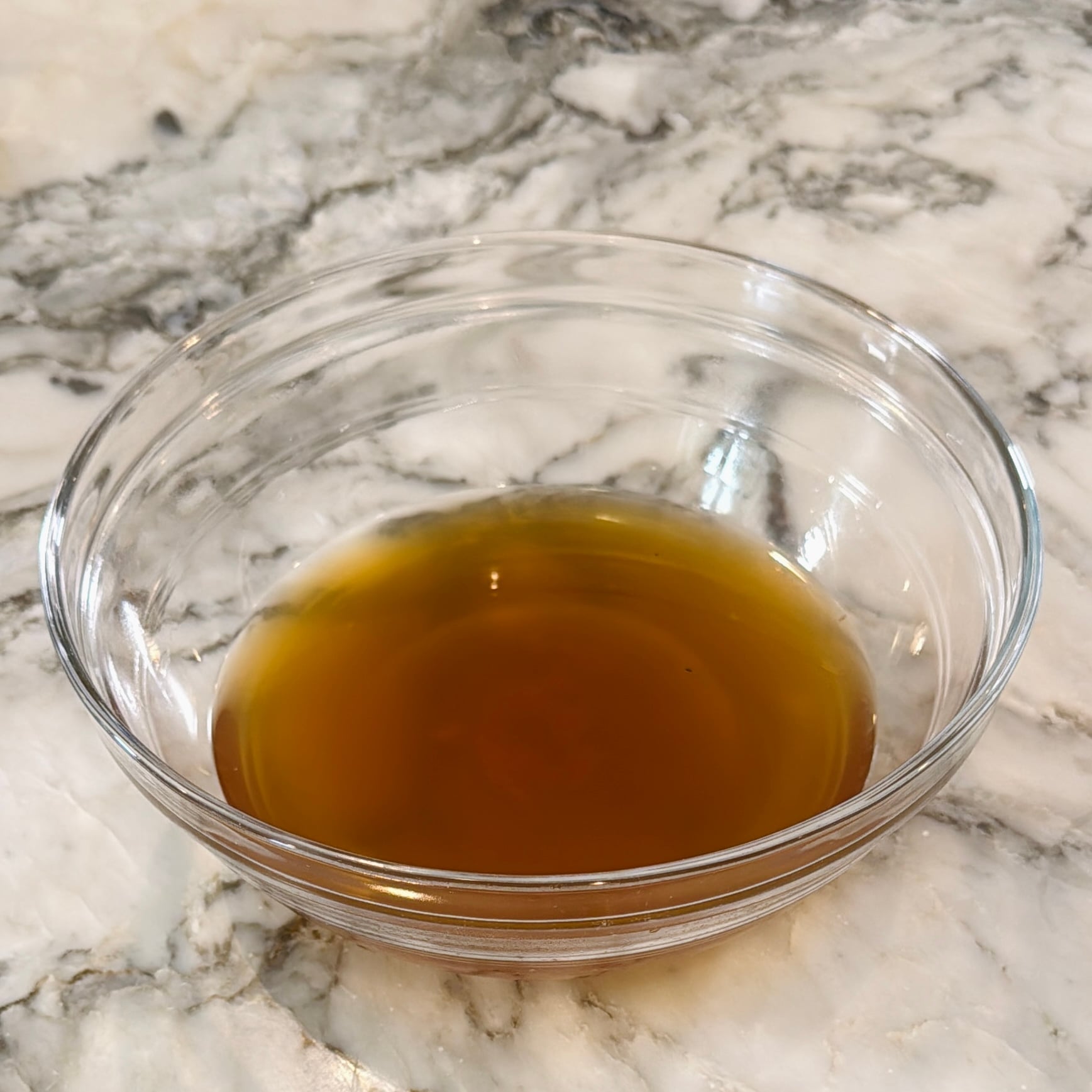 A glass bowl containing amber liquid on a marble countertop.